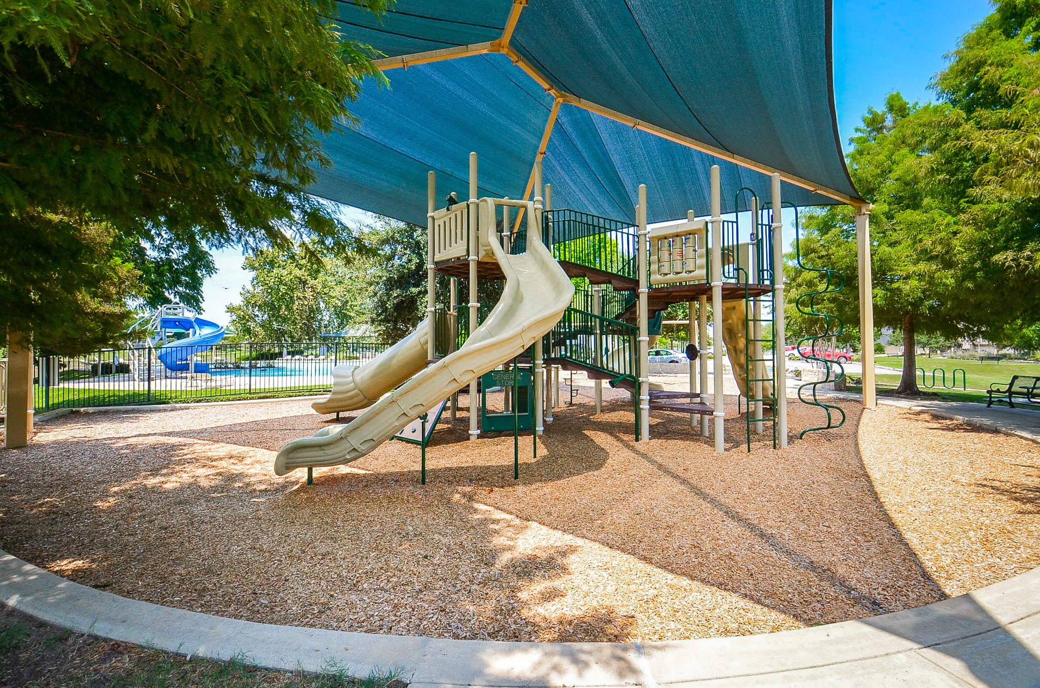 A well-shaded playground with slides and climbing structures, perfect for family fun, nestled in a beautifully landscaped park setting.