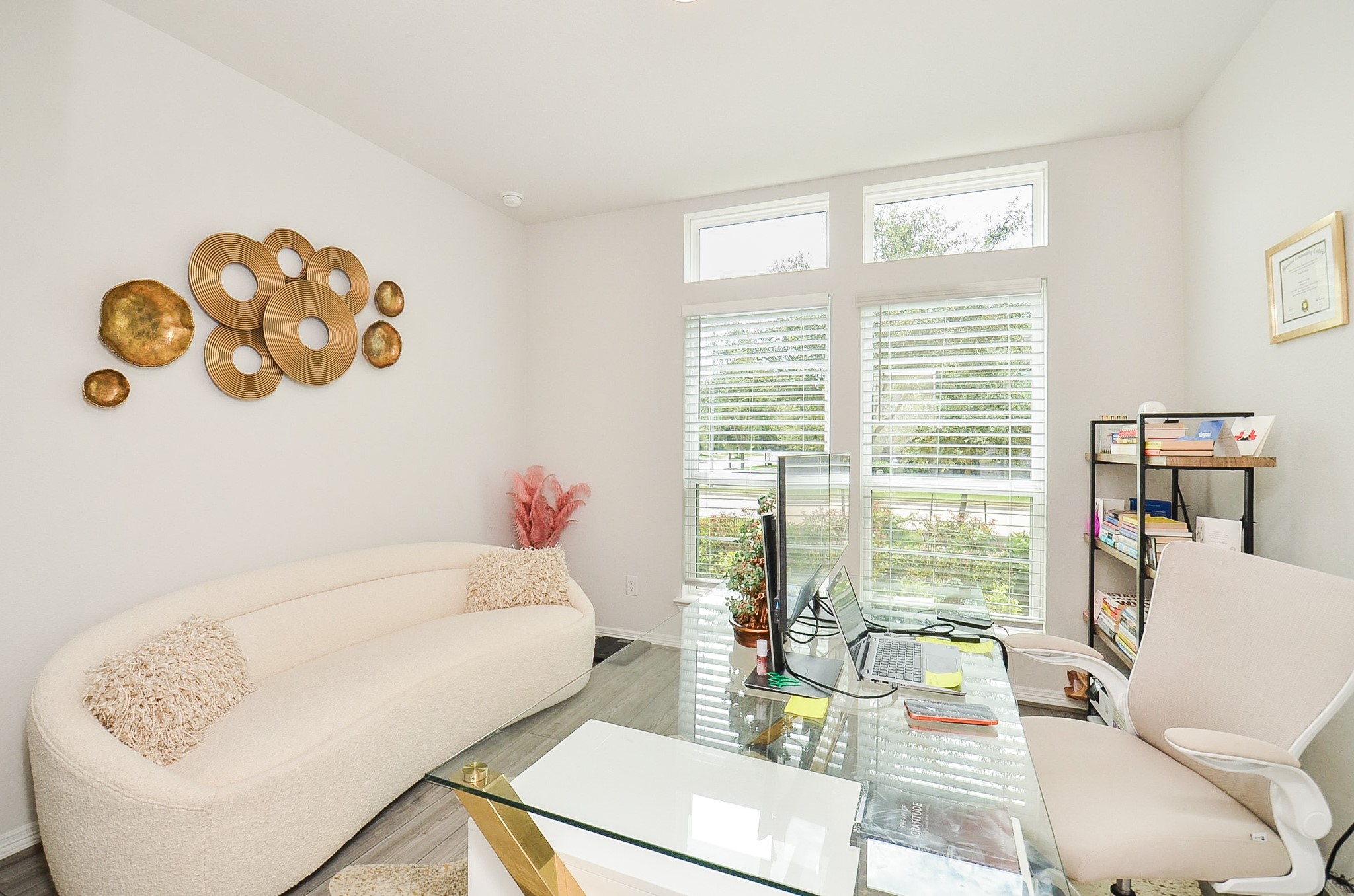 Bright and inviting home office featuring large windows with elegant shutters, a contemporary glass desk, and modern decor for a stylish workspace.
