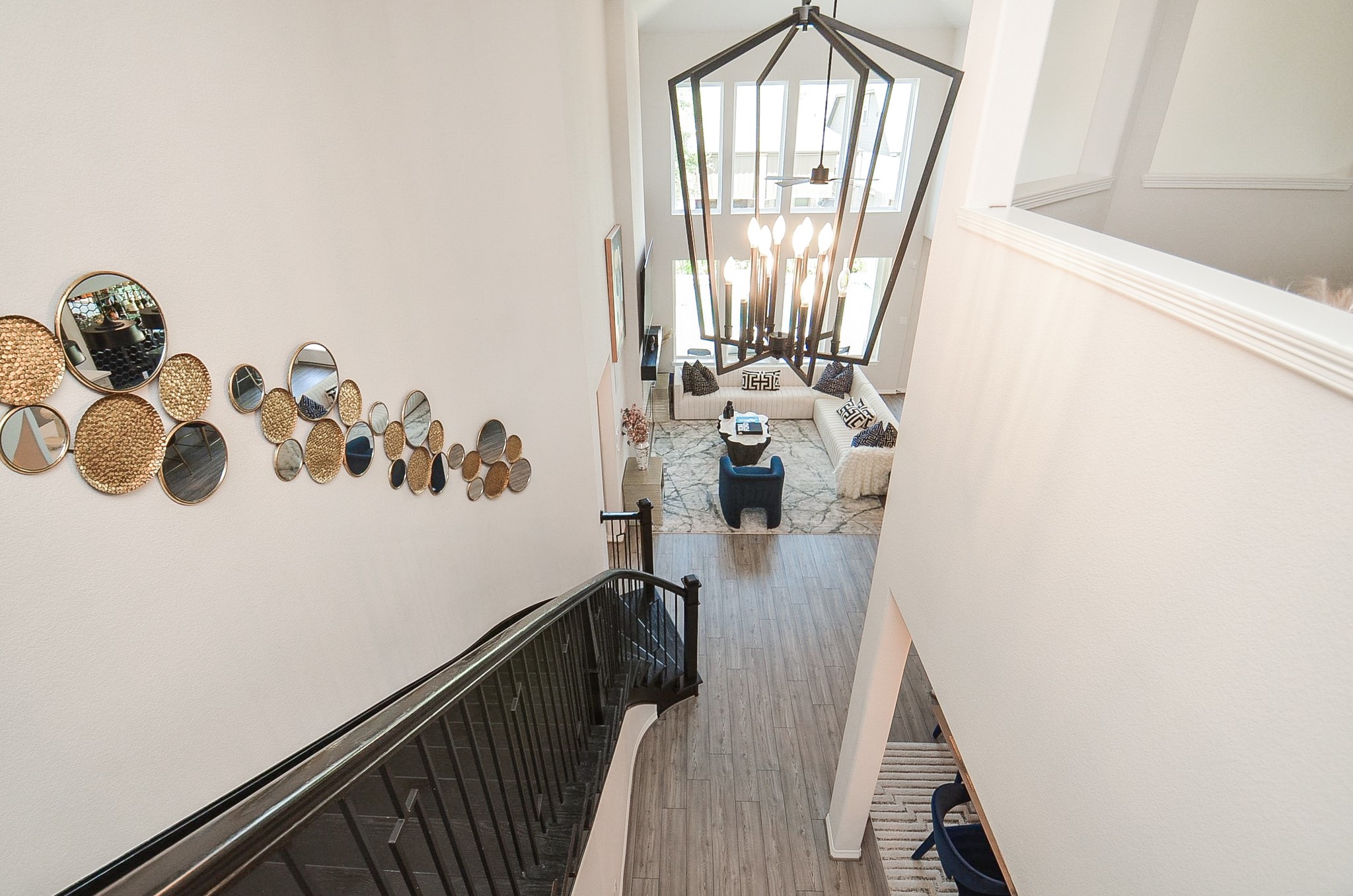 Elegant two-story foyer with a striking modern chandelier, artistic wall accents, and a view of the spacious, sunlit living area below.