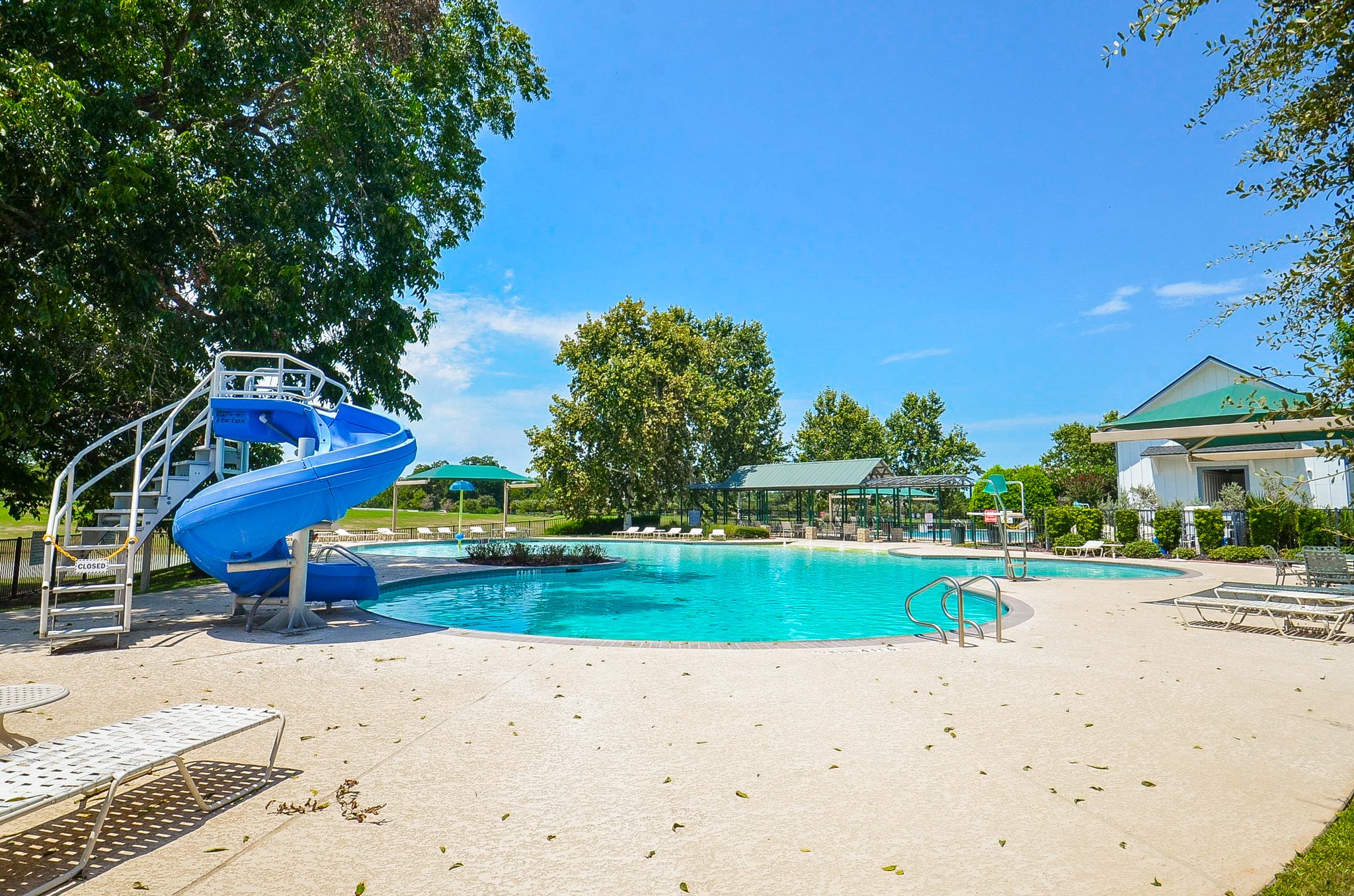 Enjoy outdoor leisure with a spacious pool featuring a fun water slide, surrounded by lush greenery and ample seating.