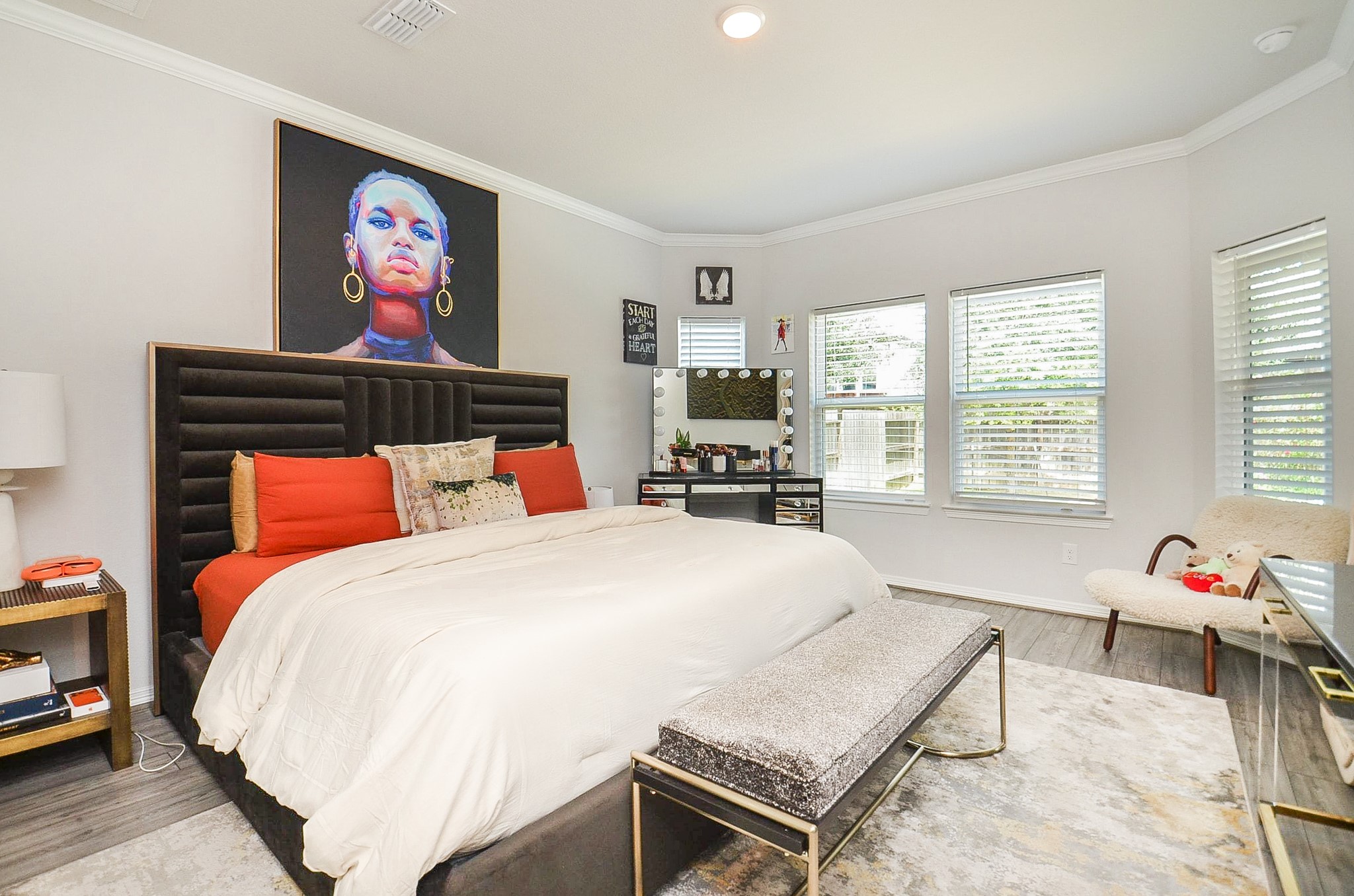 Spacious and stylish bedroom featuring a plush bed with bold accents, modern decor, and abundant natural light from multiple windows.