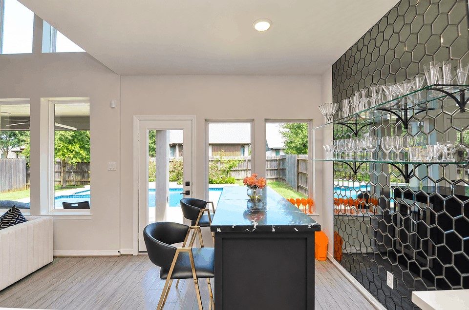Stylish home bar with sleek black hexagonal backsplash, well-stocked glass shelves, and a chic counter overlooking the backyard pool area. Ideal for entertaining. Stylish home bar with sleek black hexagonal backsplash, well-stocked glass shelves, and a chic counter overlooking the backyard pool area. Ideal for entertaining.