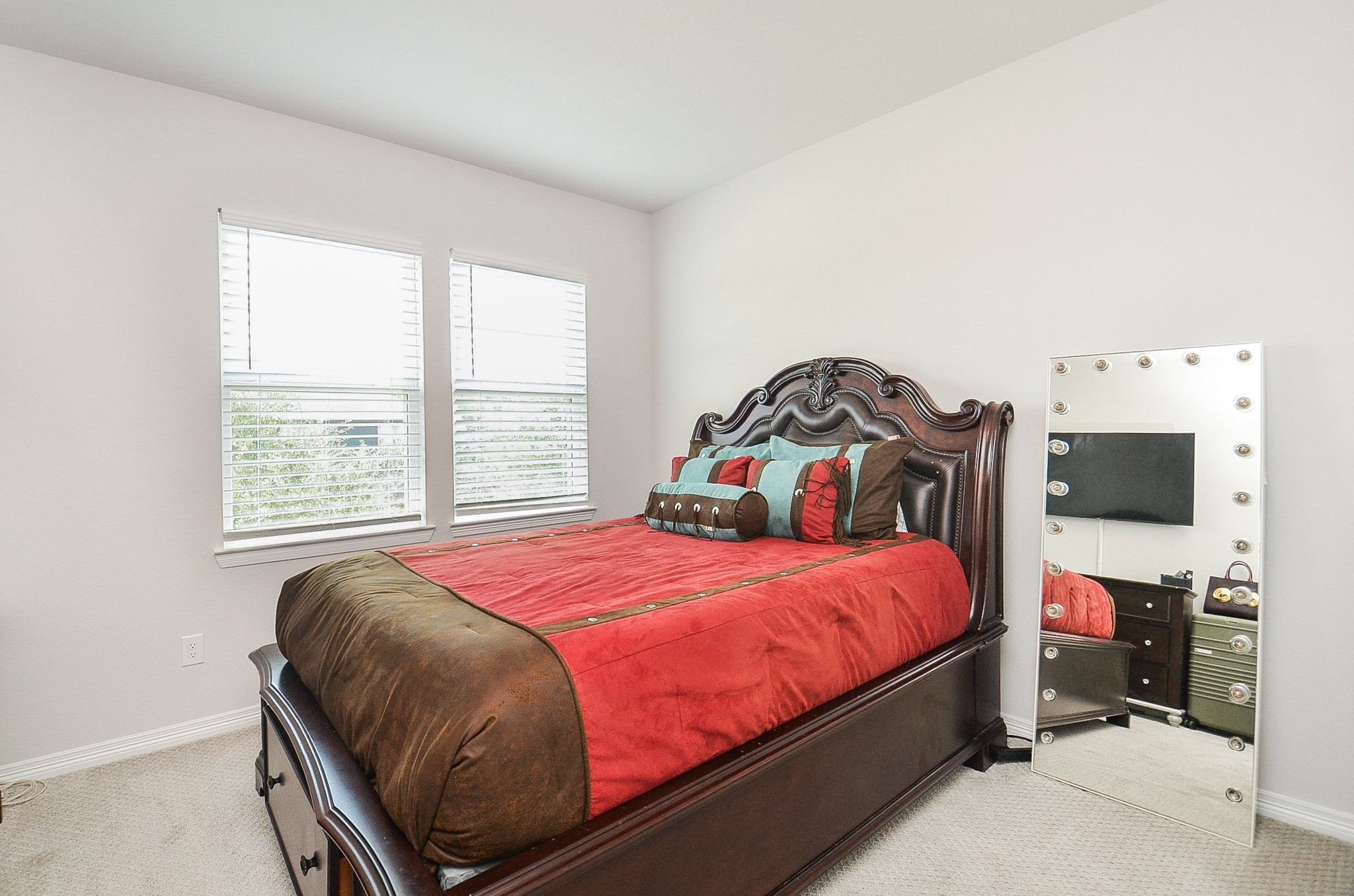 Cozy bedroom featuring a rich, wooden bed frame with elegant detailing, complemented by vibrant bedding and natural light from dual windows, creating a warm and inviting atmosphere.