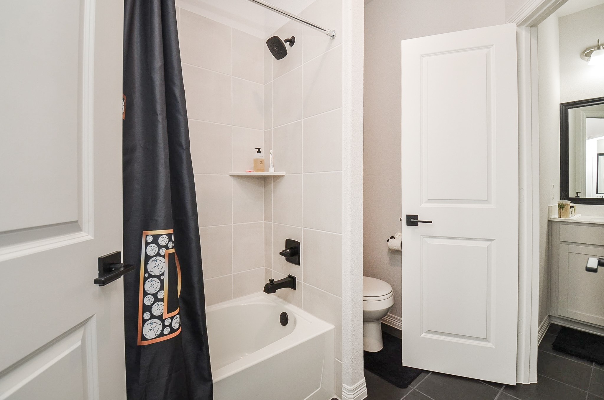 Chic bathroom featuring a modern tub and shower combo with sleek black fixtures, complemented by a stylish vanity area with ample lighting.