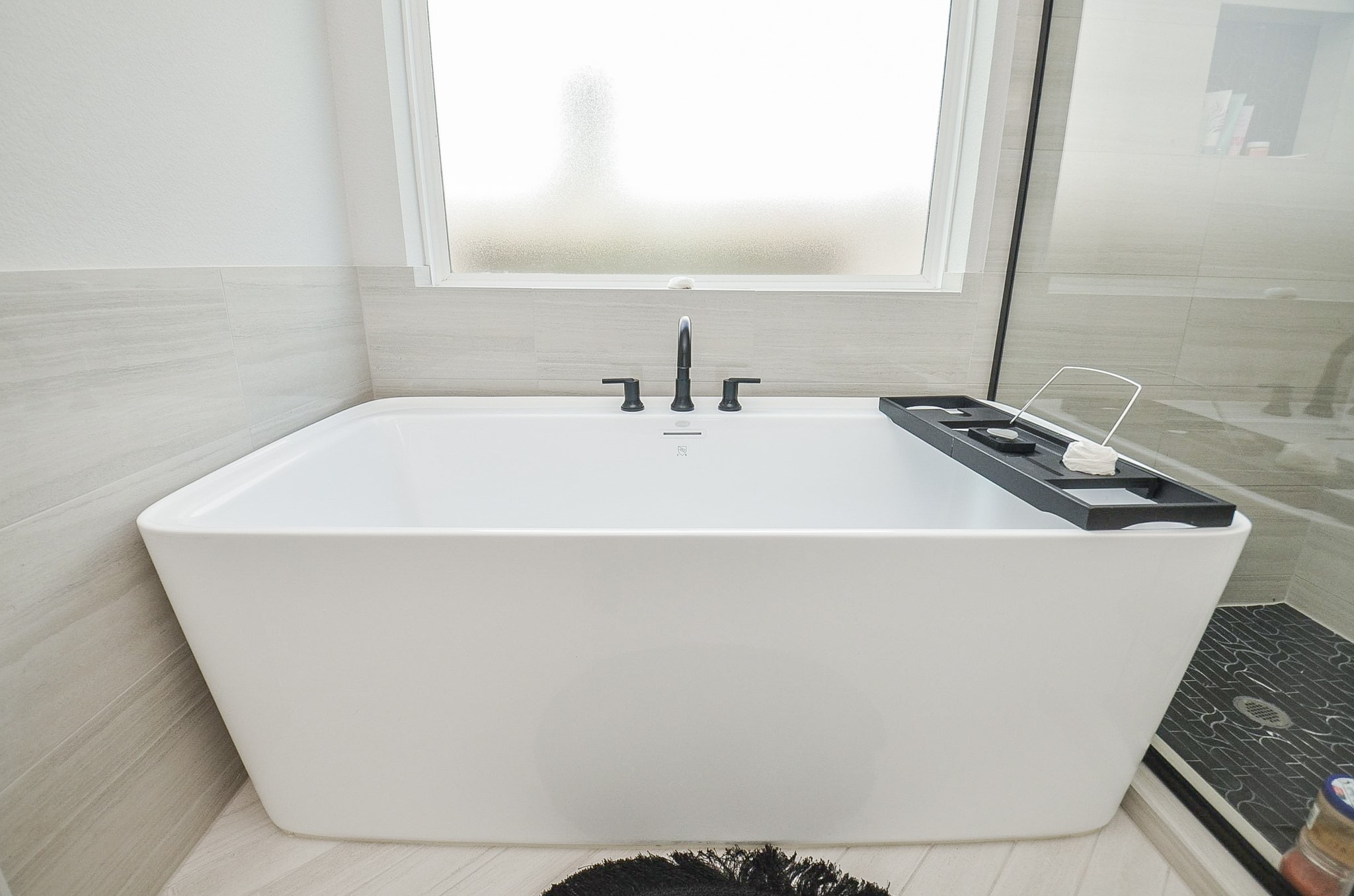 Experience ultimate relaxation in this modern bathroom featuring a sleek, freestanding soaking tub with elegant fixtures, complemented by stylish tile flooring and a frosted window for privacy.