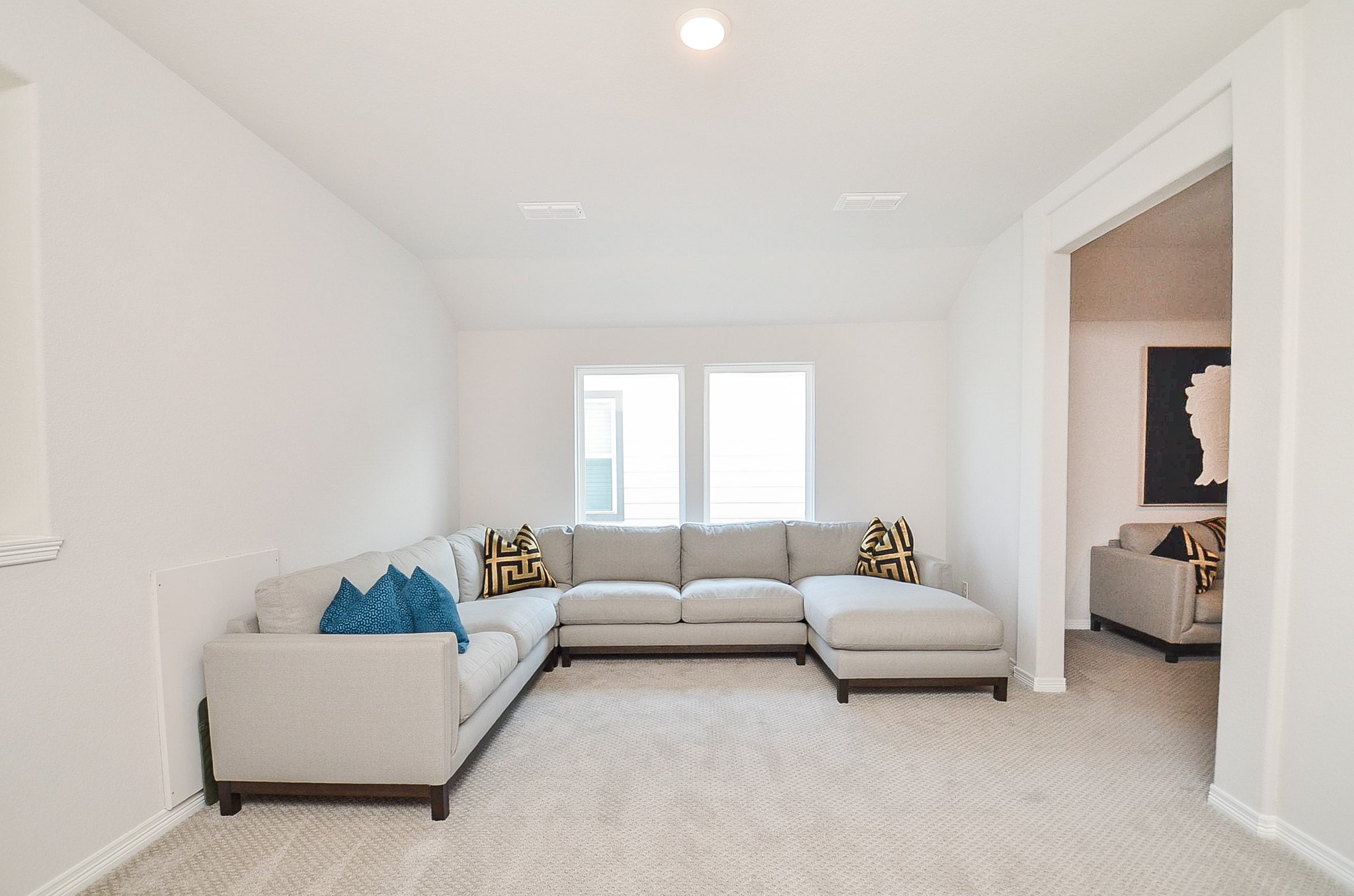 Spacious living area featuring a cozy sectional sofa, plush carpeting, and abundant natural light from two large windows.