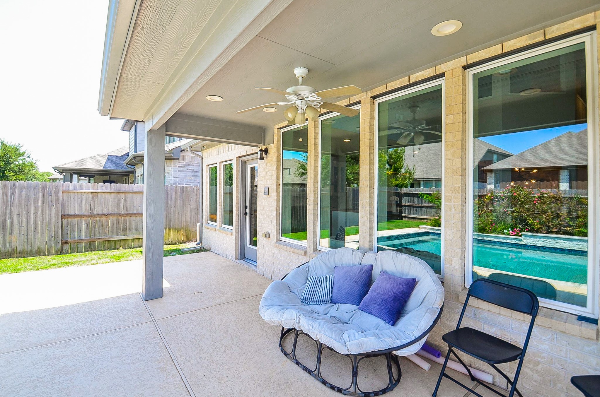 Charming covered patio with a cozy seating area, ceiling fan, and views of the sparkling backyard pool, perfect for relaxation and entertaining.