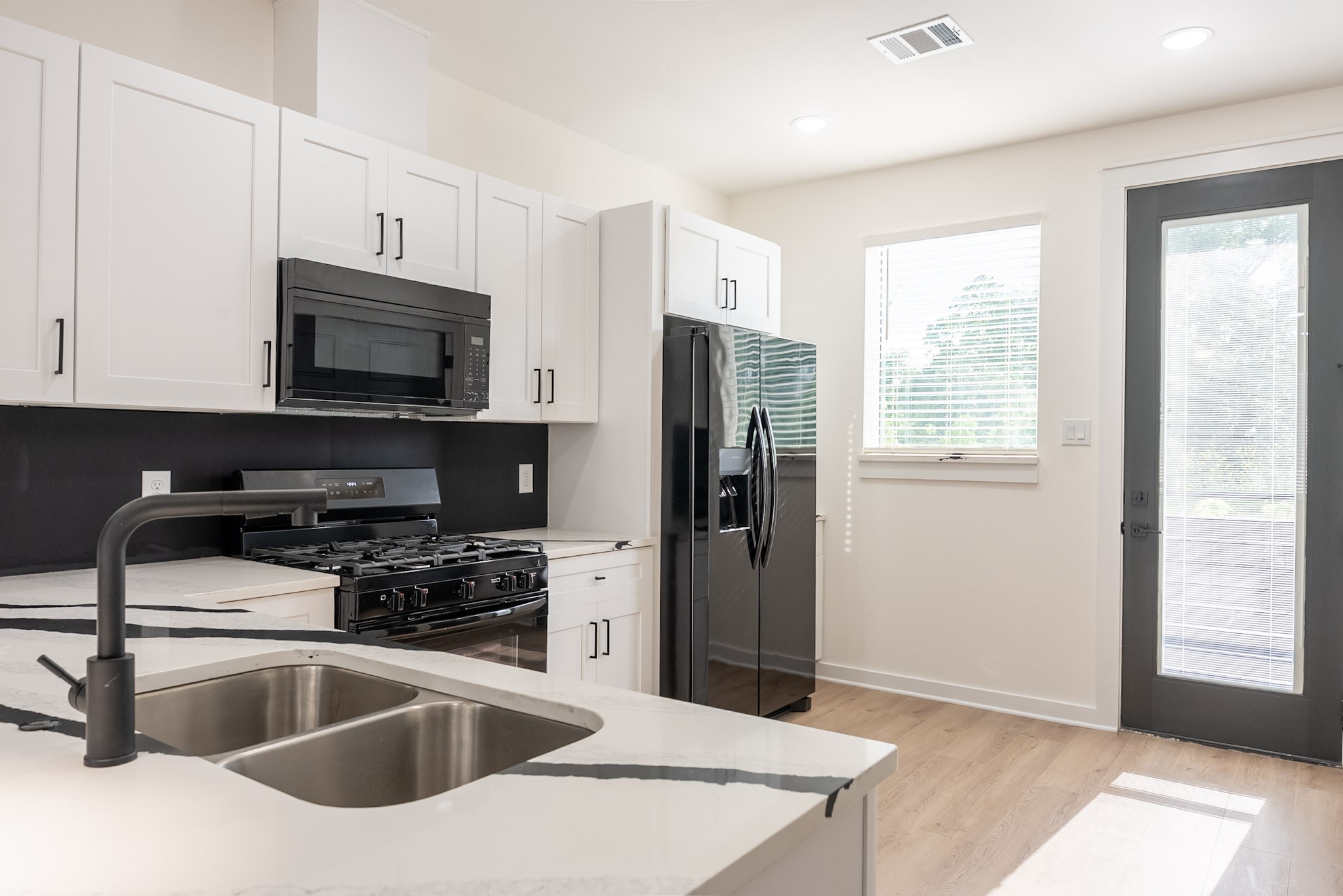 Modern kitchen featuring sleek black appliances, elegant white cabinetry, and a stylish quartz countertop with a dual sink.