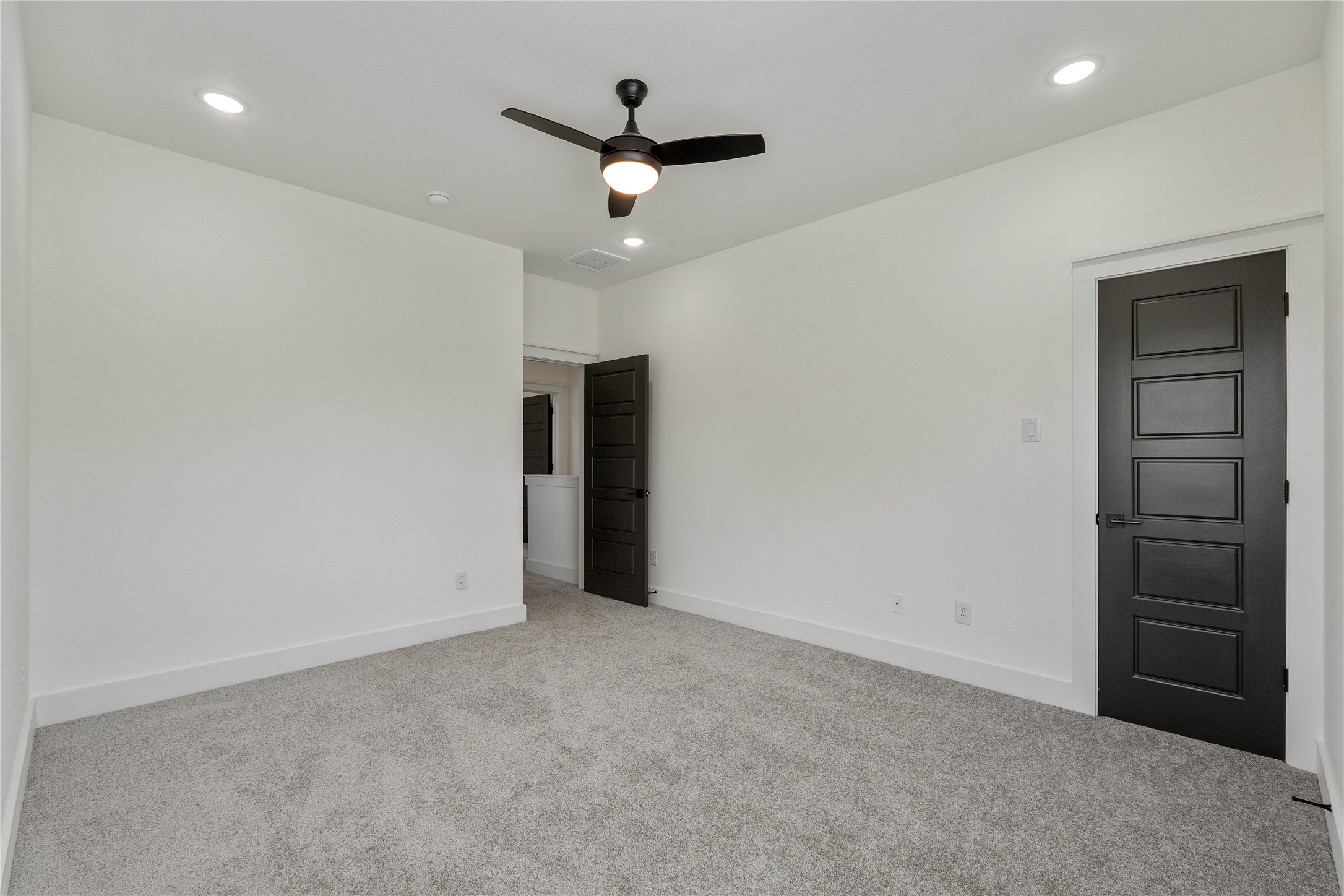 Spacious, light filled room with plush carpeting, modern ceiling fan, and sleek black doors creating a sophisticated contrast.
