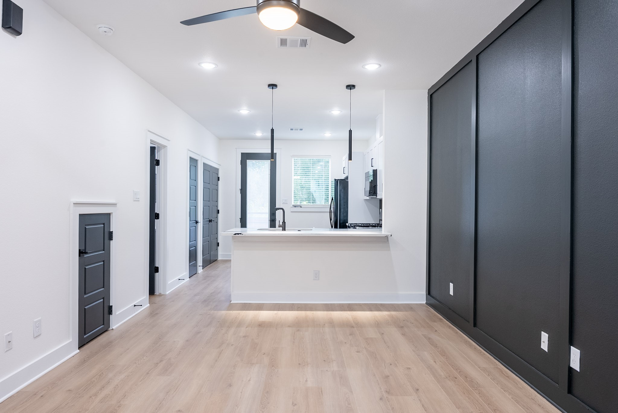 Stylish open concept kitchen and living area featuring modern light fixtures, and warm wood flooring for a contemporary feel.