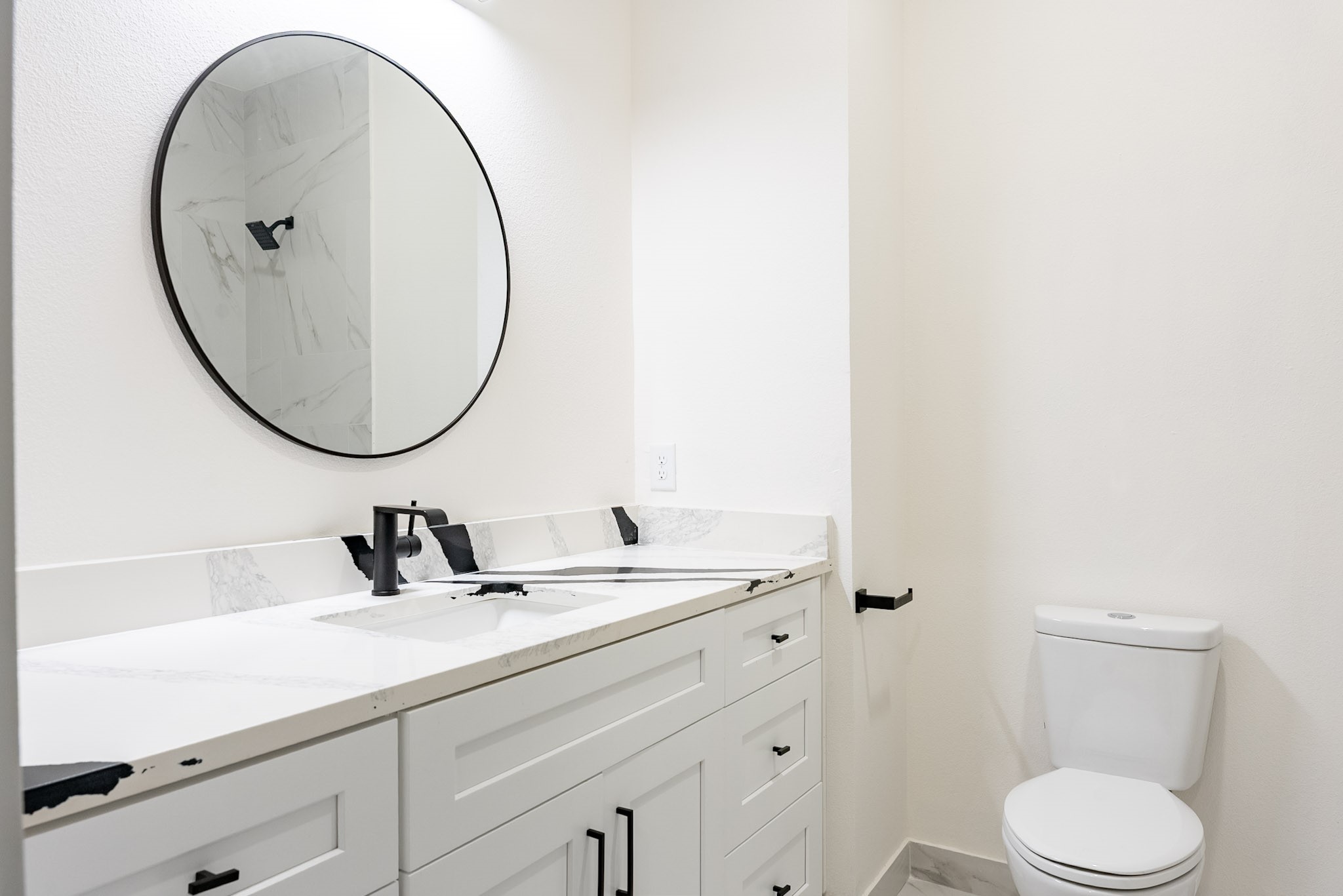 Modern bathroom featuring a sleek vanity with quartz countertop, stylish black fixtures, and a large round mirror for an elegant touch.
