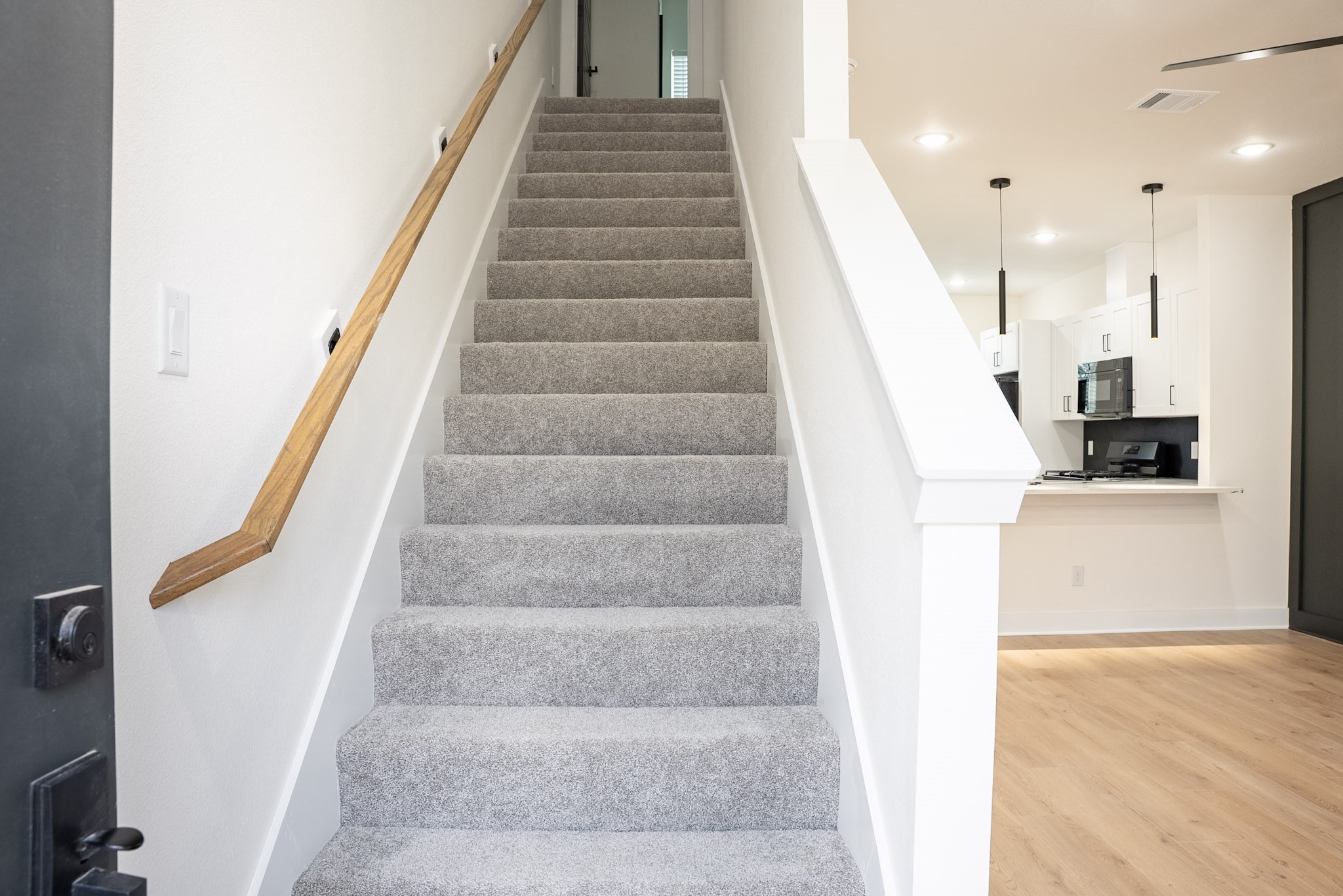 Bright entryway featuring a modern staircase with plush carpeting, leading to an inviting open concept kitchen with sleek white cabinetry and pendant lighting.