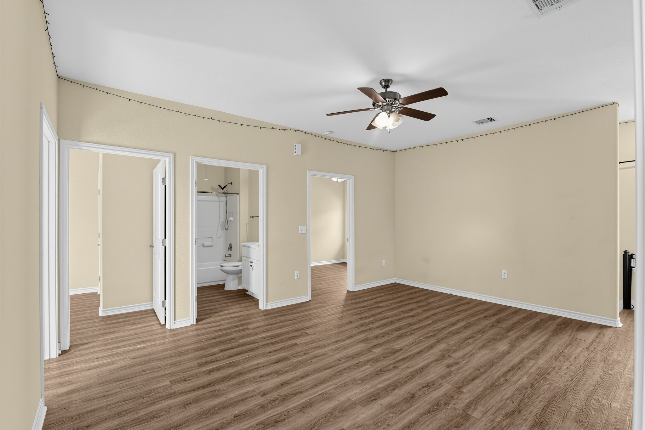 The living room features a ceiling fan with a light fixture and extensive wood laminate flooring. Two bedrooms are located on either side of the full bathroom.