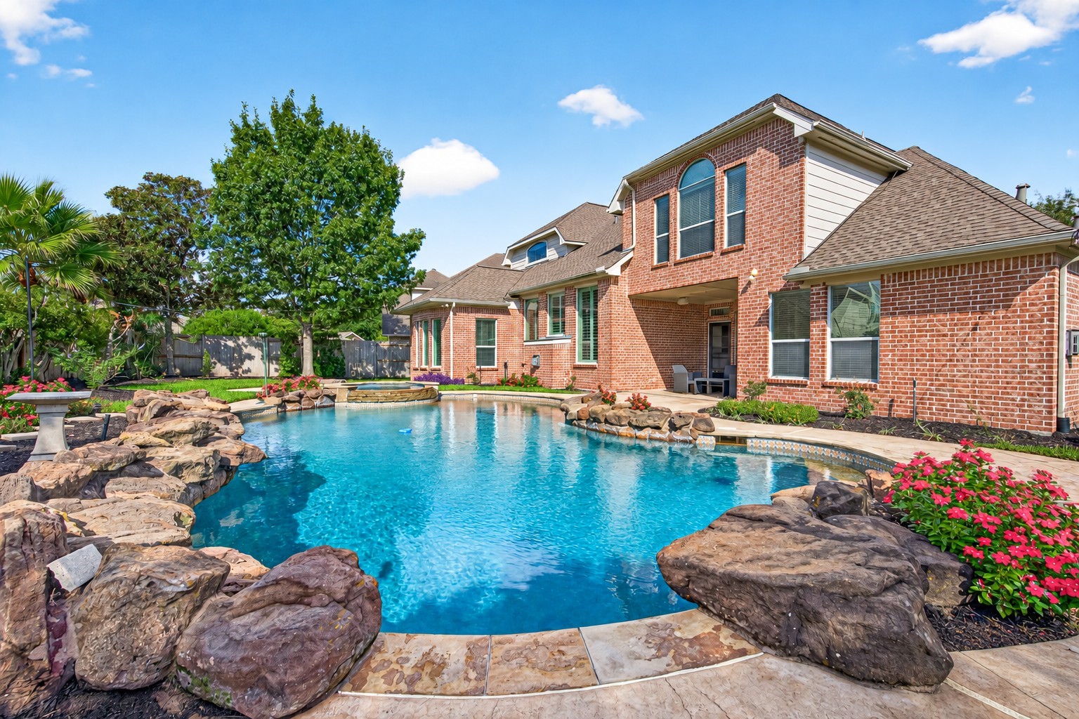 Stunning backyard oasis featuring a sparkling pool with natural stone accents, surrounded by lush landscaping and a beautiful brick home as the backdrop. Stunning backyard oasis featuring a sparkling pool with natural stone accents, surrounded by lush landscaping and a beautiful brick home as the backdrop.
