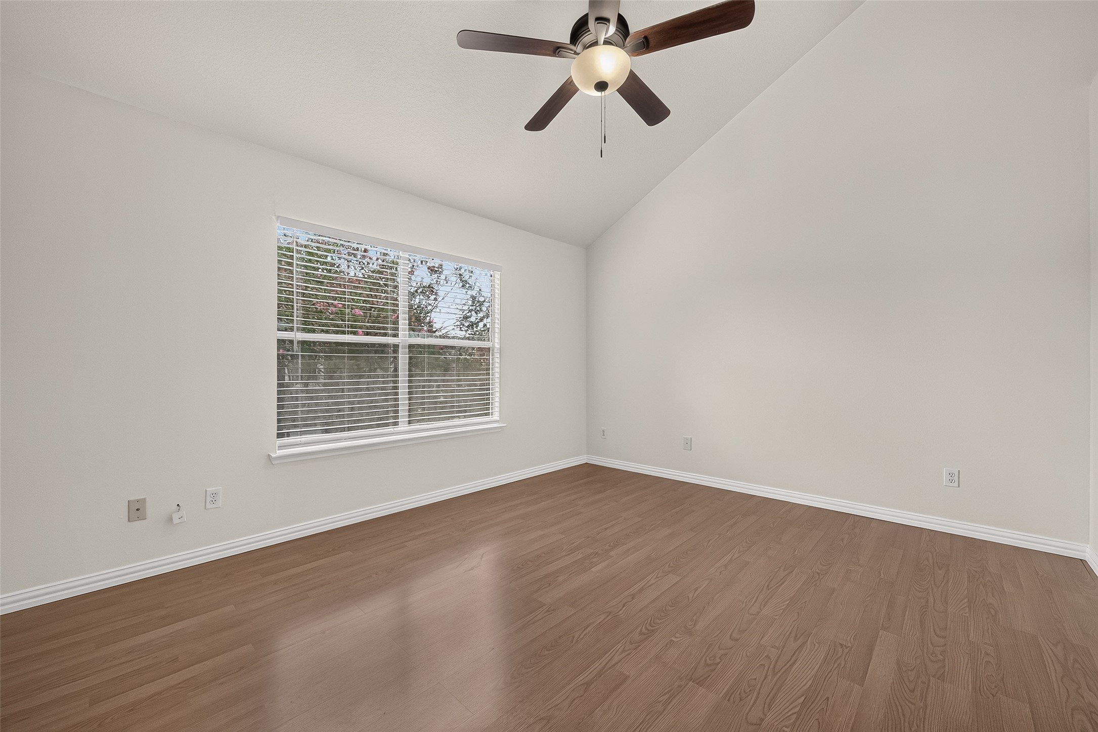 Comfortable secondary bedroom with vaulted ceiling, ceiling fan, wood-look flooring, large window, and plenty of natural light.