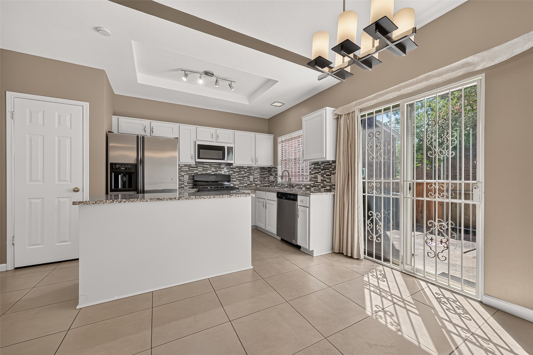 Bright, open dining and kitchen area featuring tile flooring, contemporary lighting, granite countertops, stainless-steel appliances, and direct access to the private patio.