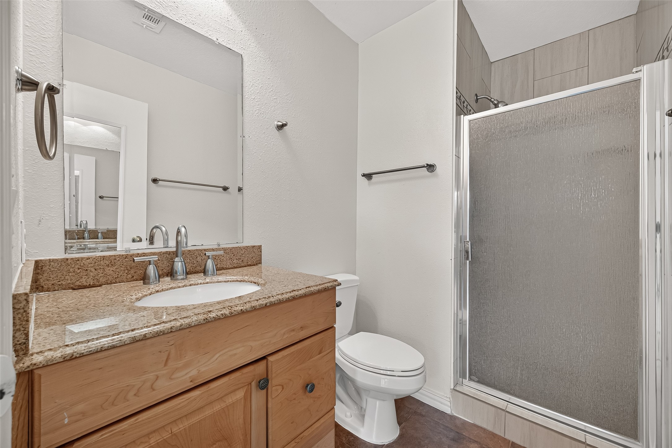 En-suite primary bath featuring granite countertop vanity and tiled shower with glass enclosure.