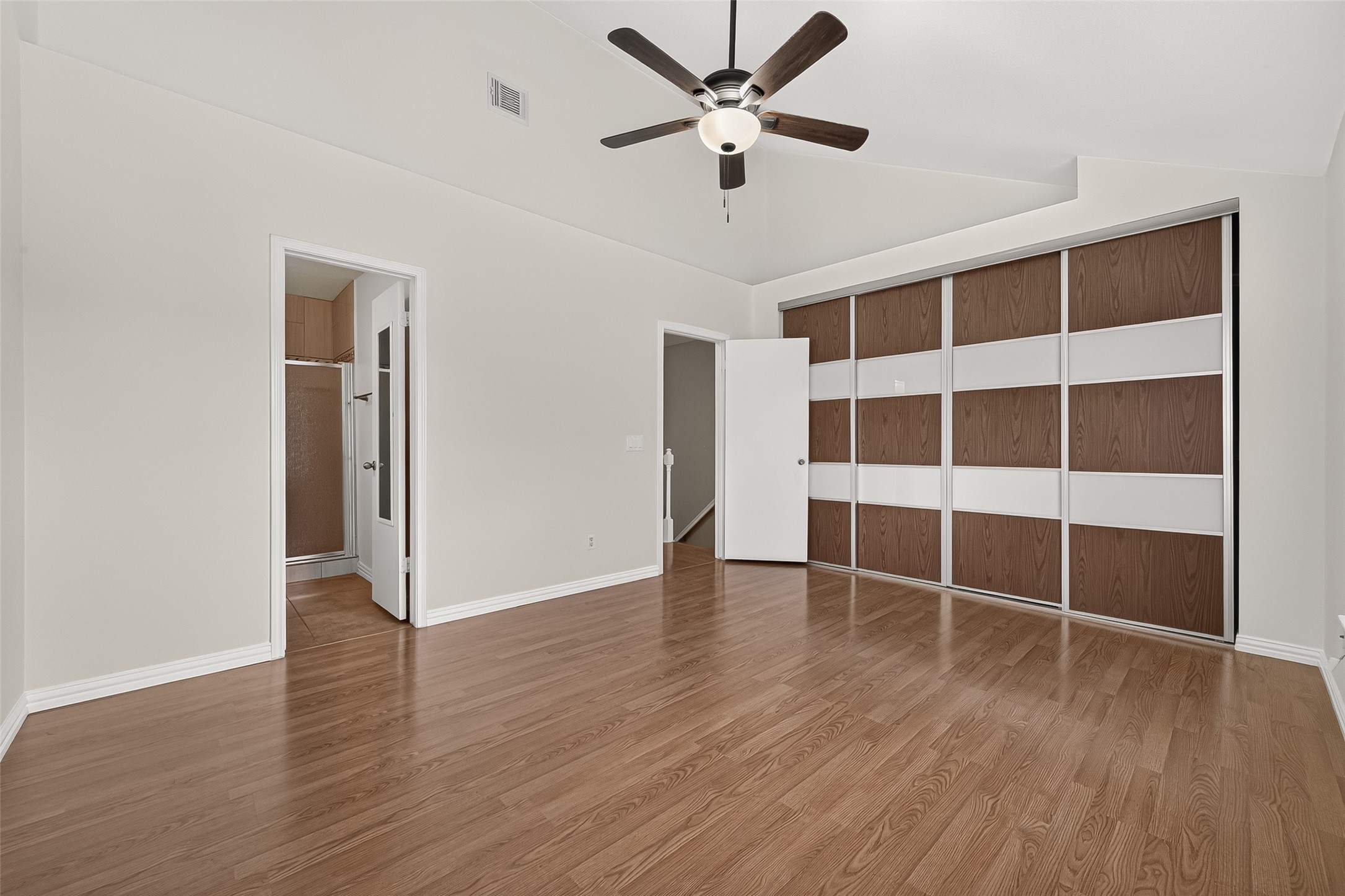 Spacious primary bedroom featuring wood-look flooring, vaulted ceiling, ceiling fan, en-suite bath access, and newly installed premium sliding closet doorsa significant recent upgrade.