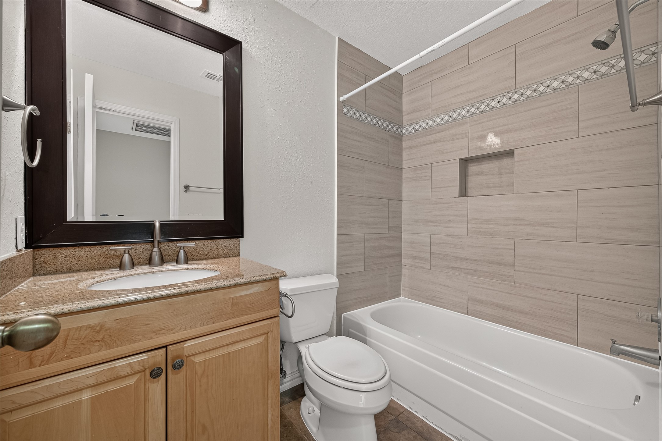 The guest bath has full bath featuring granite countertop vanity, tub/shower combination, large-format tile surround, decorative accent detailing, and built-in shower niche.