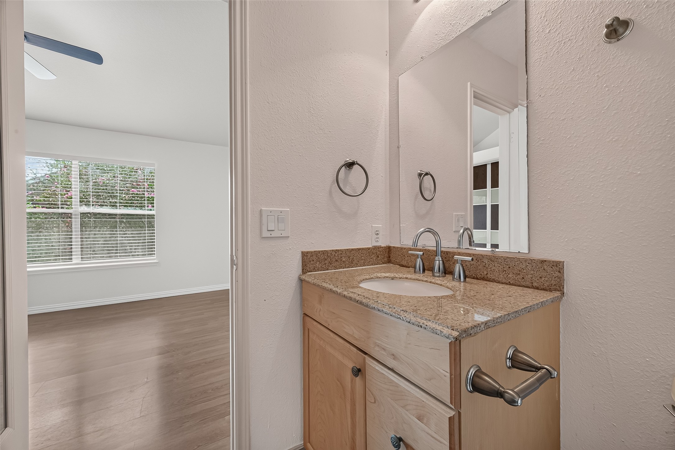 En-suite primary bath featuring granite countertop vanity, contemporary fixtures, large mirror, and convenient access from the spacious primary bedroom.