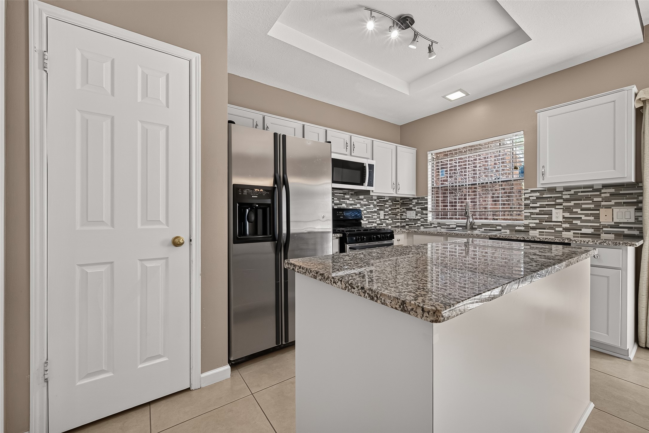Open kitchen and dining area featuring a large granite island, white cabinetry, tile flooring, modern lighting, and convenient access to the private patio.