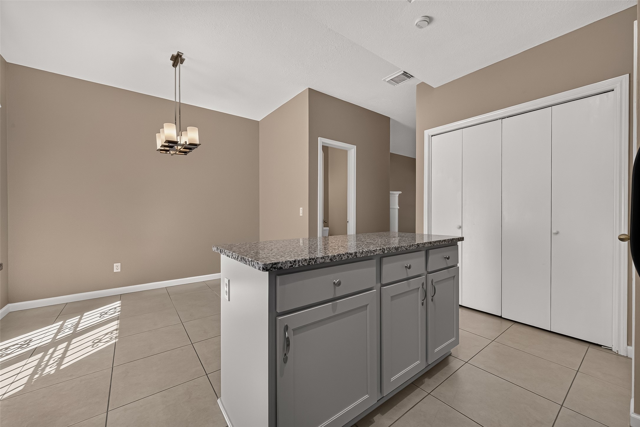 Open dining area adjacent to the kitchen with granite-topped island, generous storage, neutral finishes, and modern lighting.