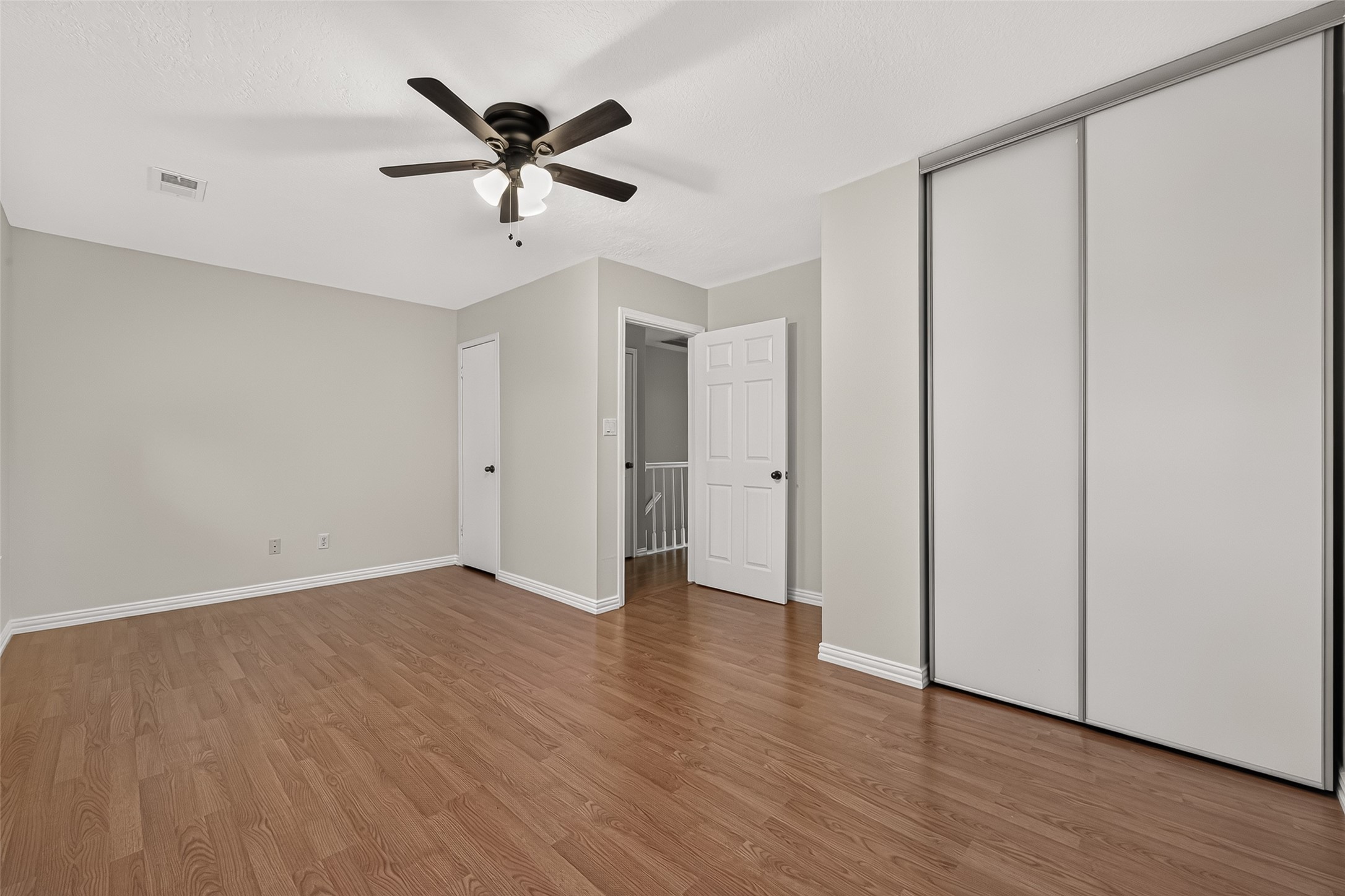 Spacious secondary bedroom featuring wood-look flooring, ceiling fan, and newly installed contemporary sliding closet doors providing a clean, updated appearance.