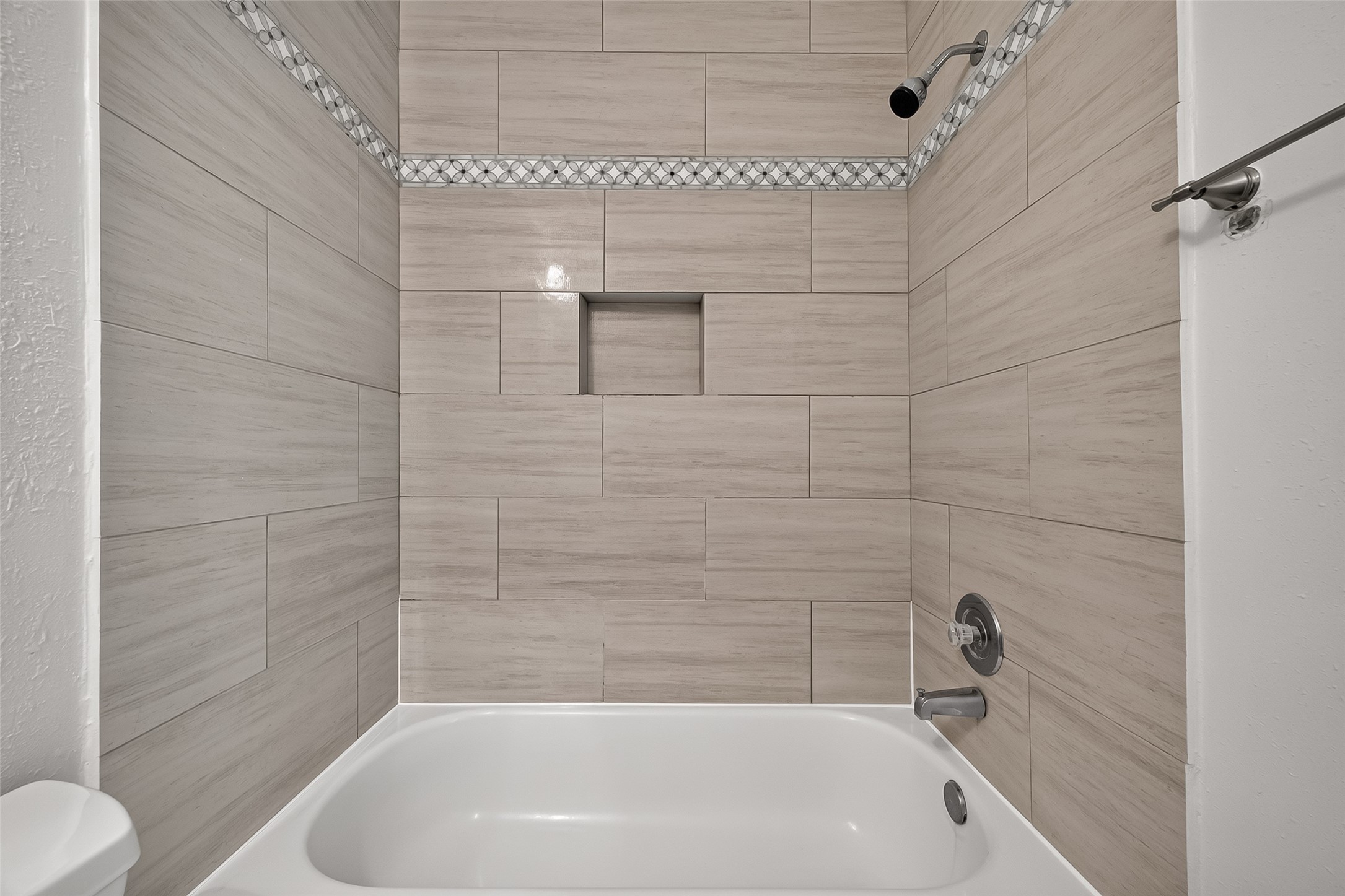 Attractive tub/shower combination surrounded by large-format tile with decorative accent border and convenient built-in shower niche.