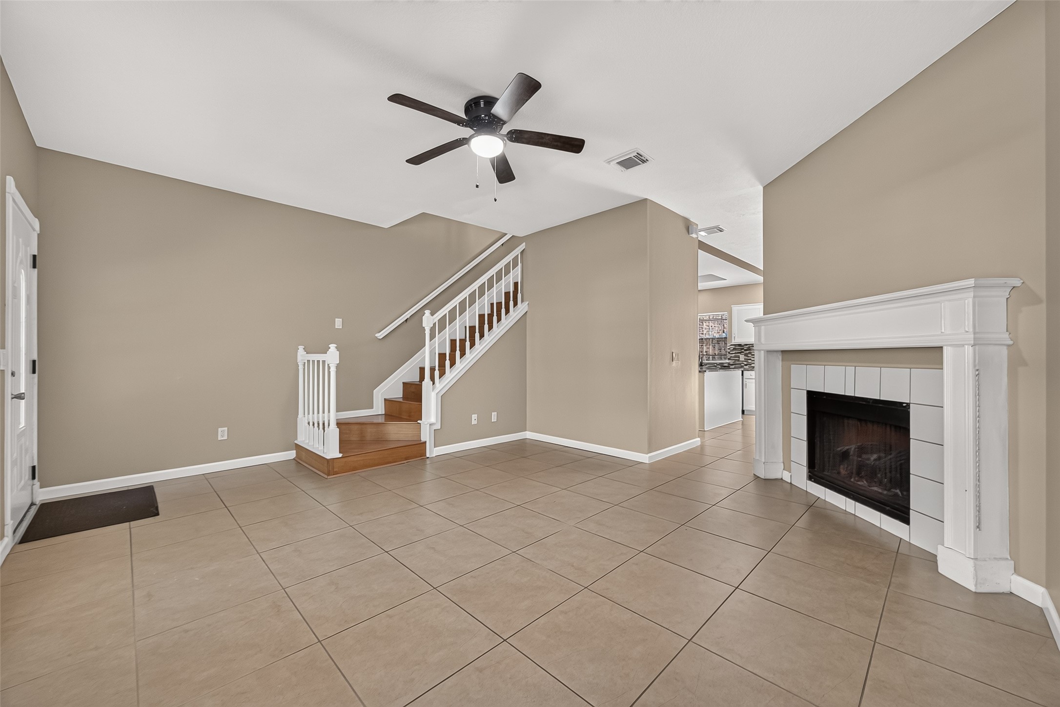 Open living area with fireplace, neutral finishes, tile flooring, and easy flow toward the kitchen and staircase. Open living area with fireplace, neutral finishes, tile flooring, and easy flow toward the kitchen and staircase.
