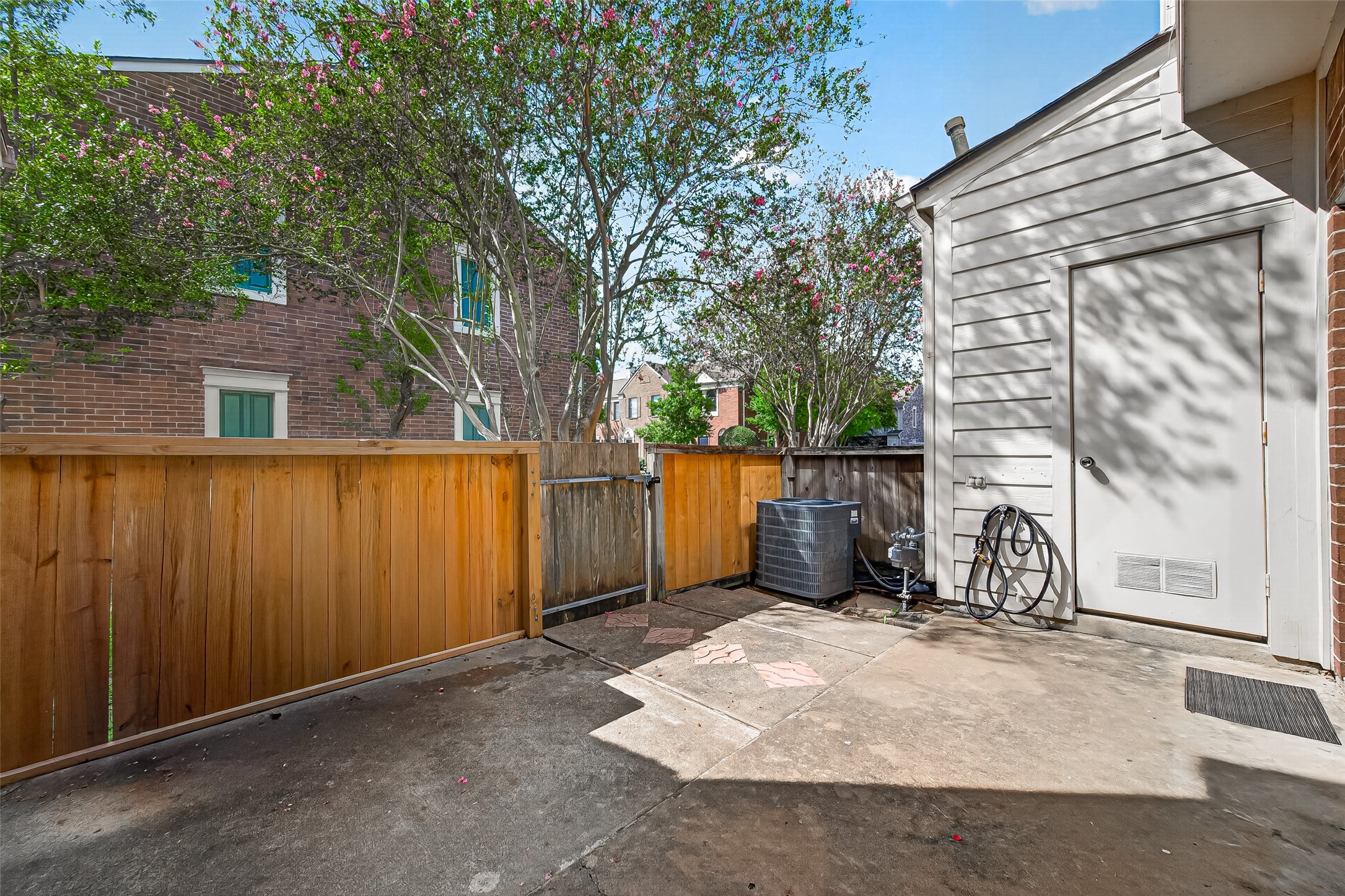 Fenced private patio with mature trees nearby, outdoor utility area, and convenient exterior storage access.