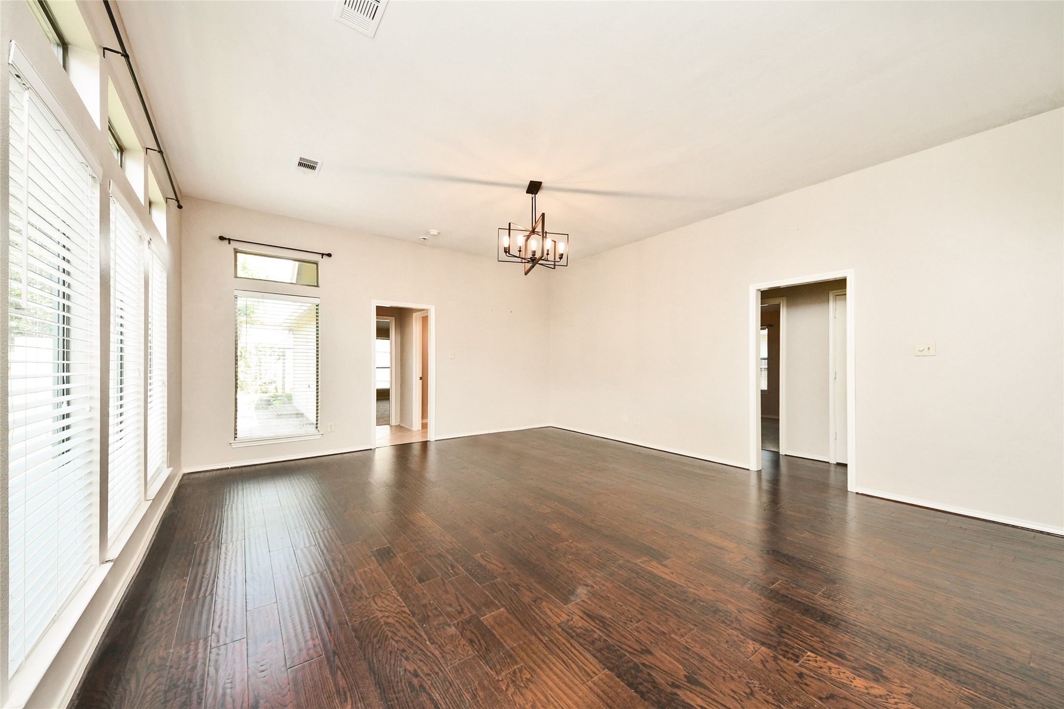 Spacious living area featuring elegant dark hardwood floors, abundant natural light from large windows, and a stylish modern chandelier.