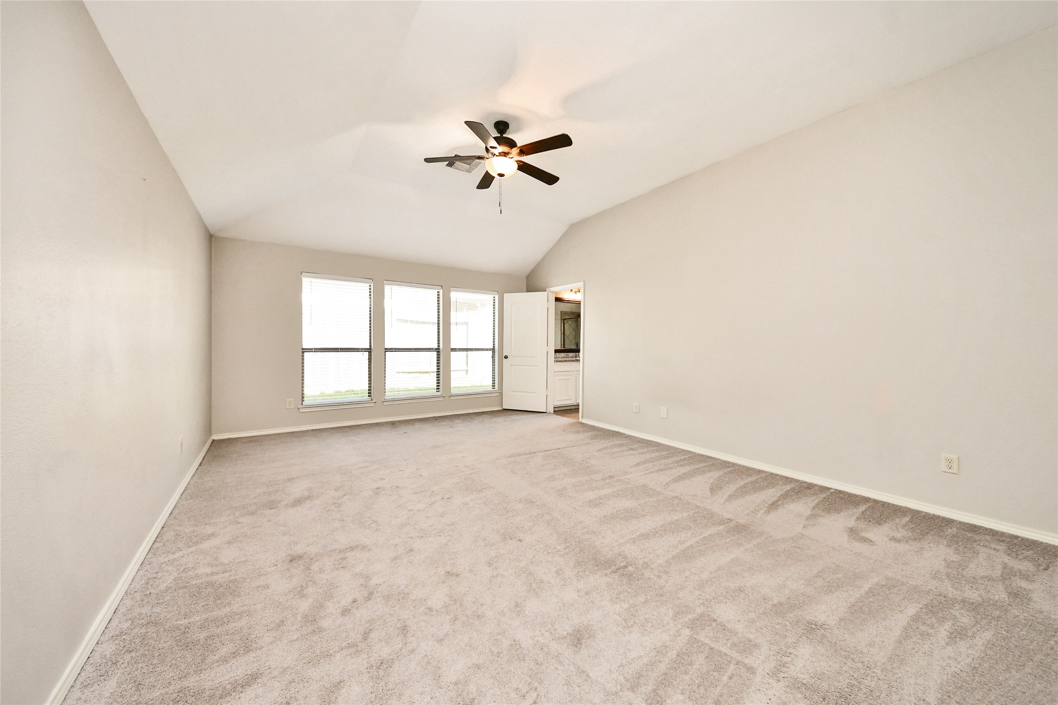 Spacious living area with vaulted ceilings, a modern ceiling fan, and large windows offering abundant natural light.