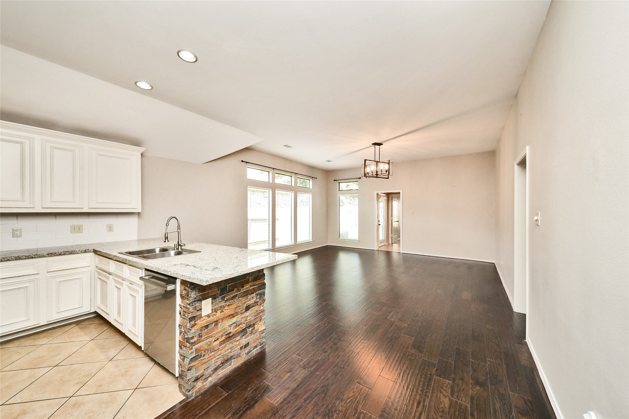 Spacious open-concept living area featuring elegant hardwood floors, a modern kitchen with granite countertops and a stone-accented island, complemented by abundant natural light from large windows.