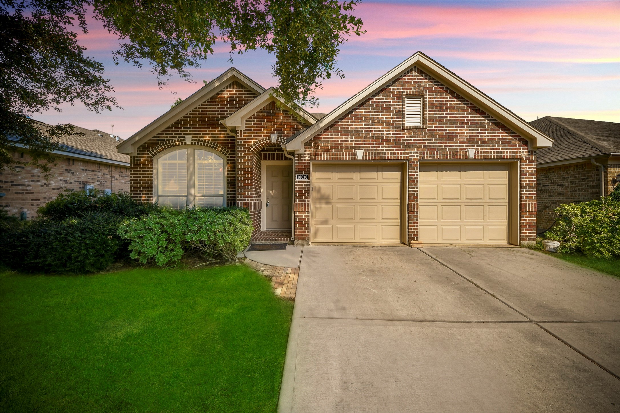 Charming brick home with a welcoming arched entryway and a spacious two-car garage, set against a lush green lawn and a serene sky.