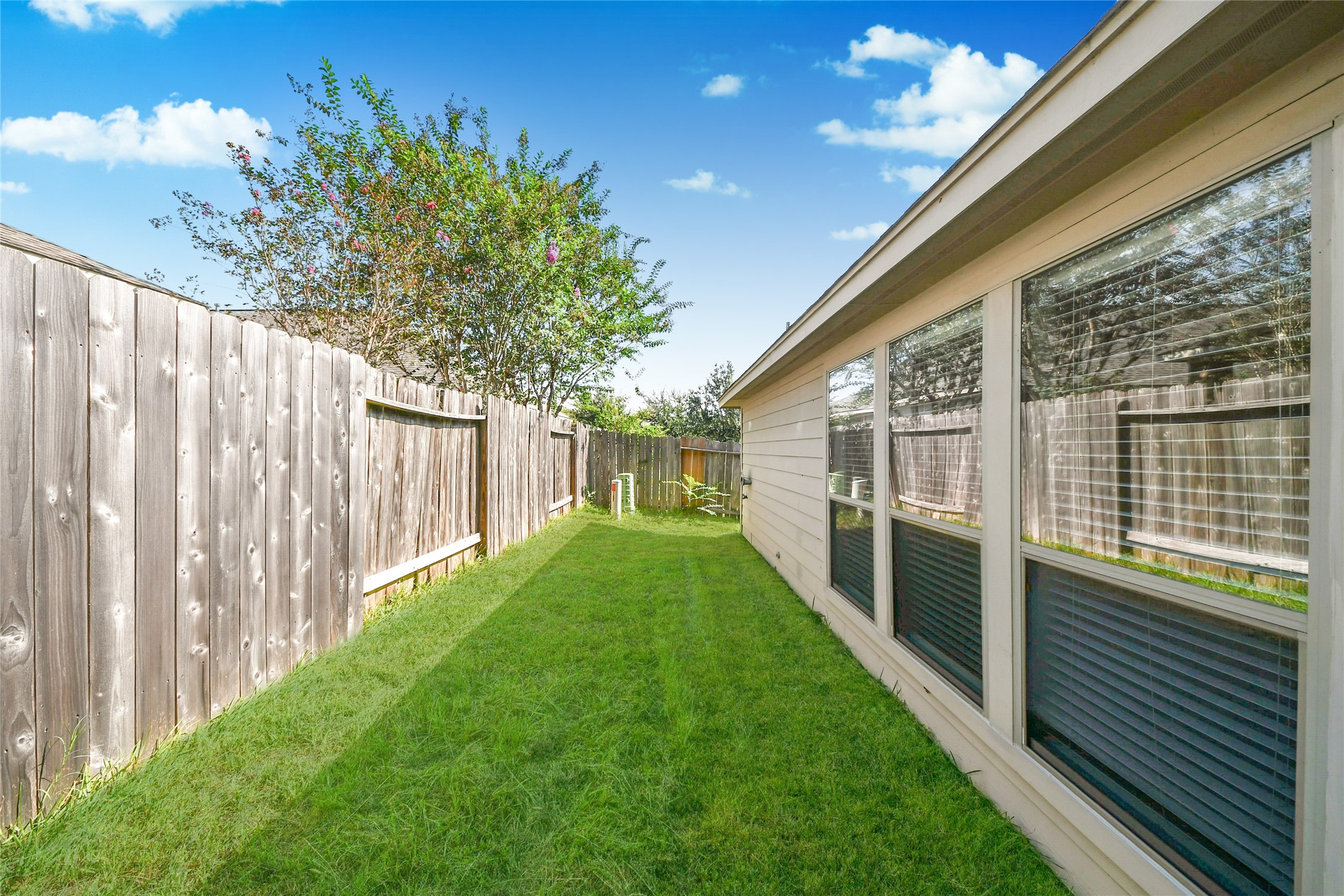 Charming side yard with lush grass, bordered by a wooden fence, perfect for a private outdoor retreat.