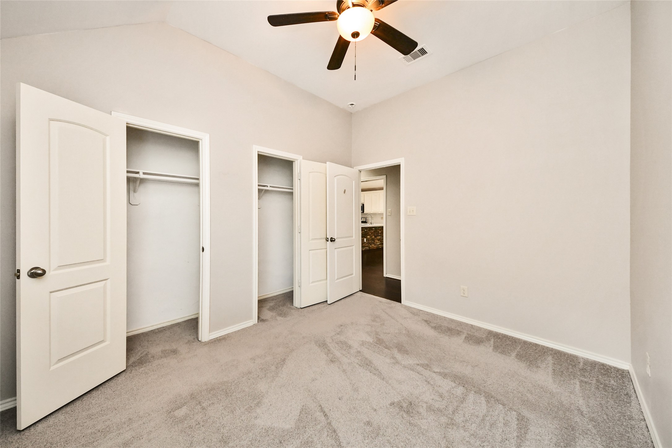 Spacious bedroom featuring soft carpeting, dual closets, and a ceiling fan for comfort and convenience.