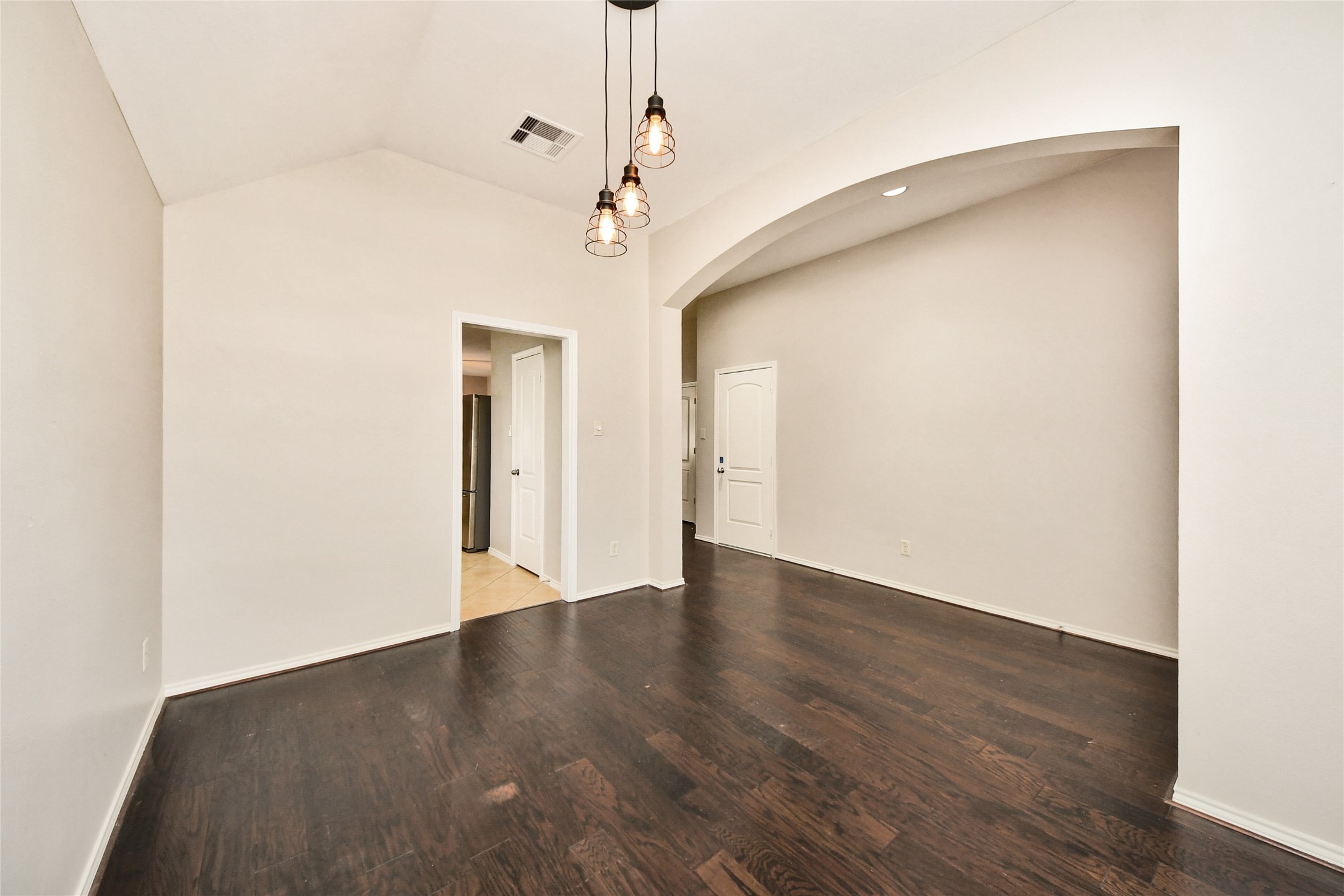 Spacious room with vaulted ceilings, elegant dark hardwood floors, and chic pendant lighting, leading to adjacent areas through stylish archways.