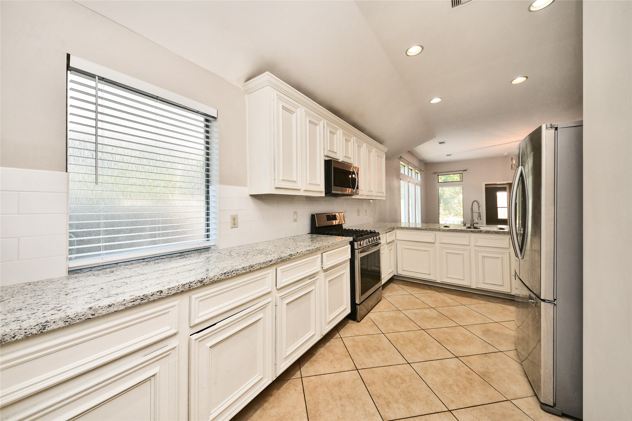 Bright and spacious kitchen featuring sleek stainless steel appliances, elegant white cabinetry, and ample natural light from large windows, perfect for culinary enthusiasts.
