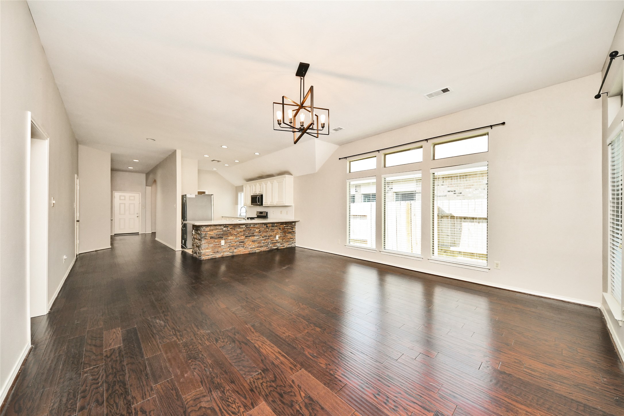 Spacious open-concept living area with rich hardwood floors, abundant natural light from large windows, and a modern kitchen featuring a stylish stone-accented island.