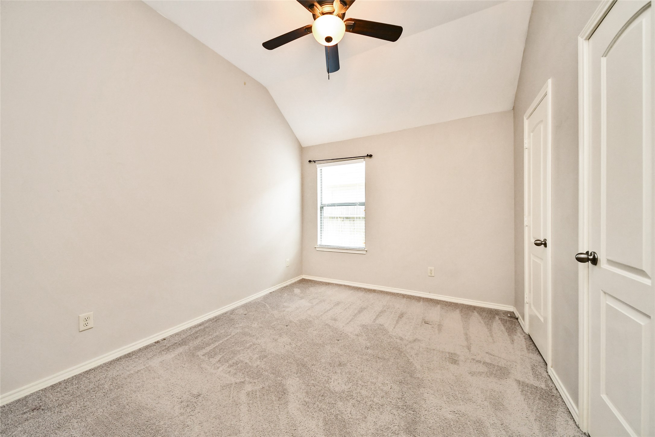 Cozy bedroom with plush carpeting, a ceiling fan, and ample natural light from a single window, perfect for restful nights.