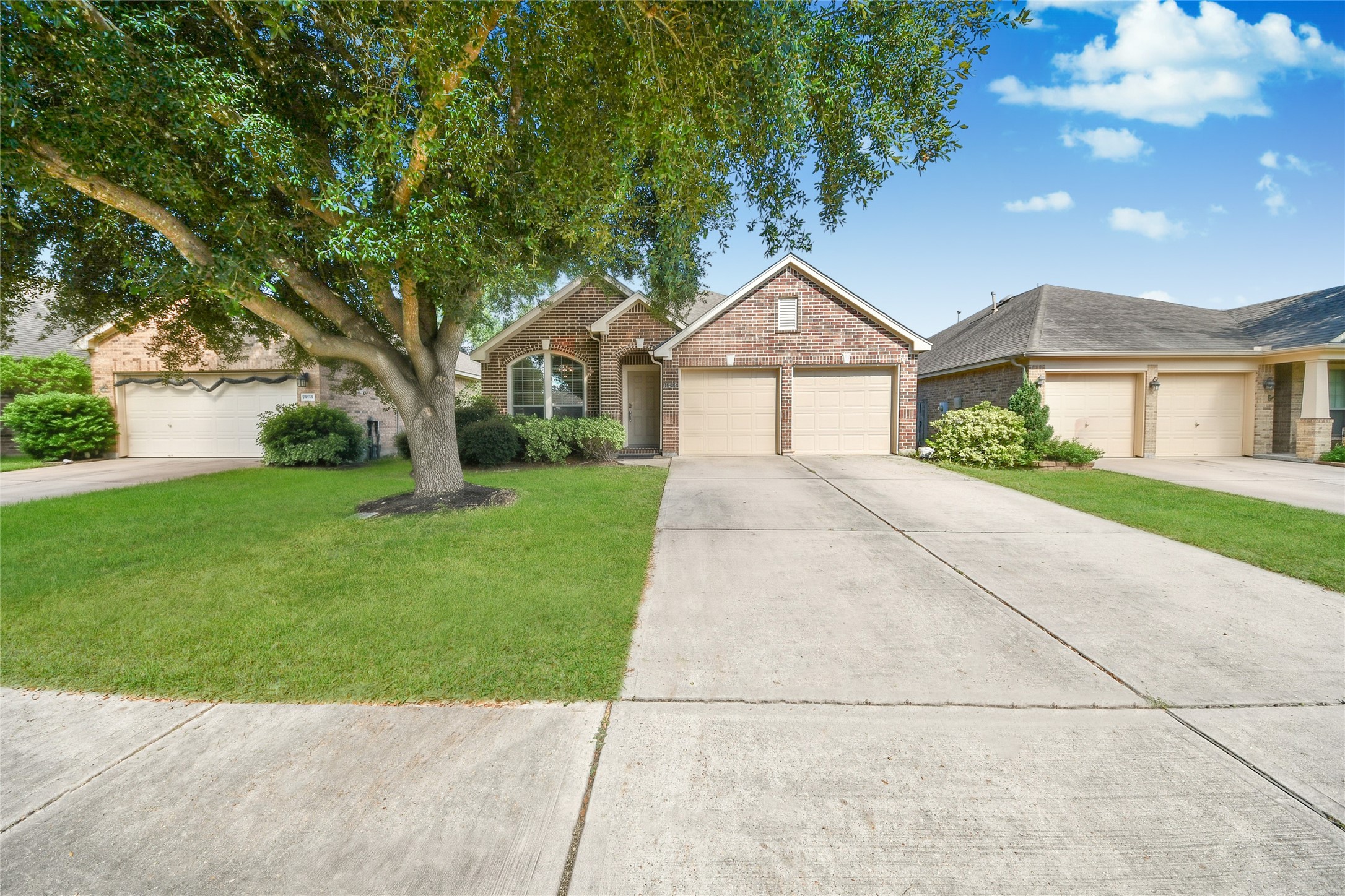Charming brick home with a spacious driveway, lush front yard, and mature tree offering ample shade.