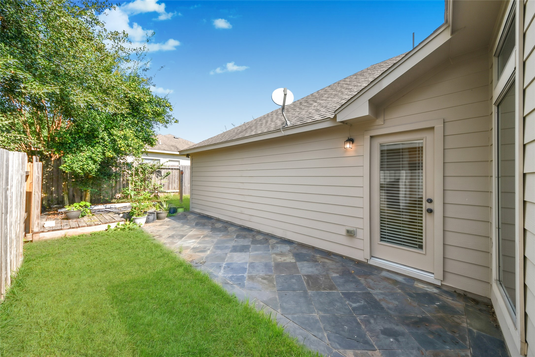 Charming backyard with a spacious stone patio, lush greenery, and a garden area perfect for outdoor relaxation and entertainment.