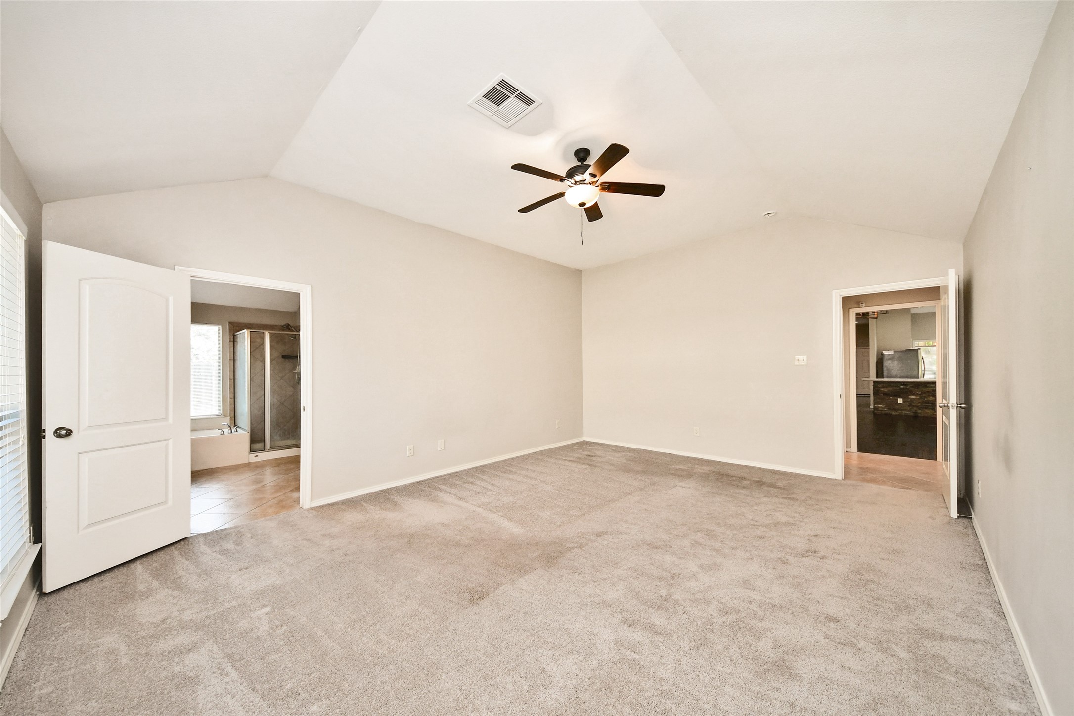 Spacious bedroom with vaulted ceilings, neutral tones, and a ceiling fan, featuring an en-suite bathroom and ample natural light.
