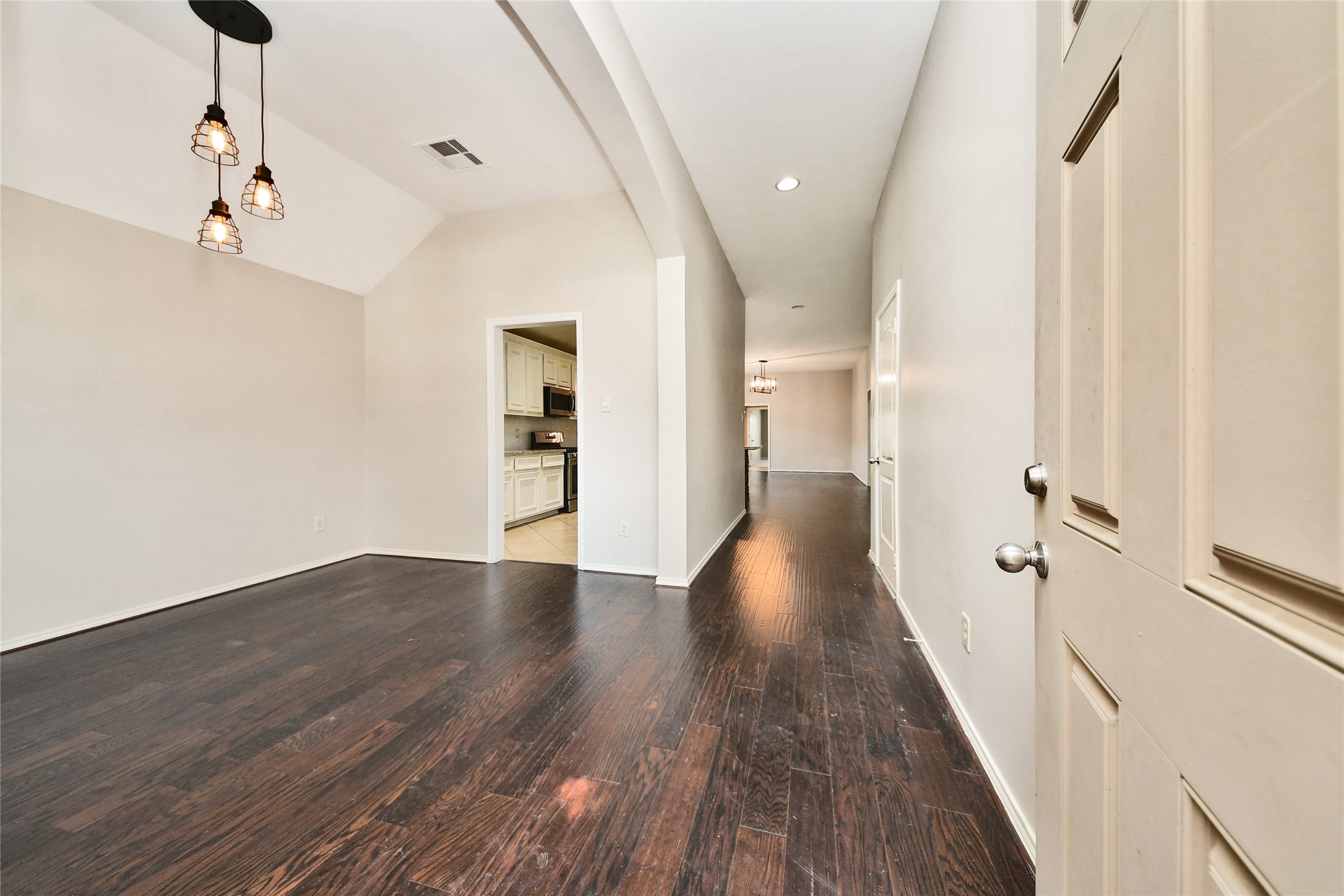 Elegant entryway with rich dark hardwood floors, modern pendant lighting, and an inviting open layout leading to the kitchen and living areas.
