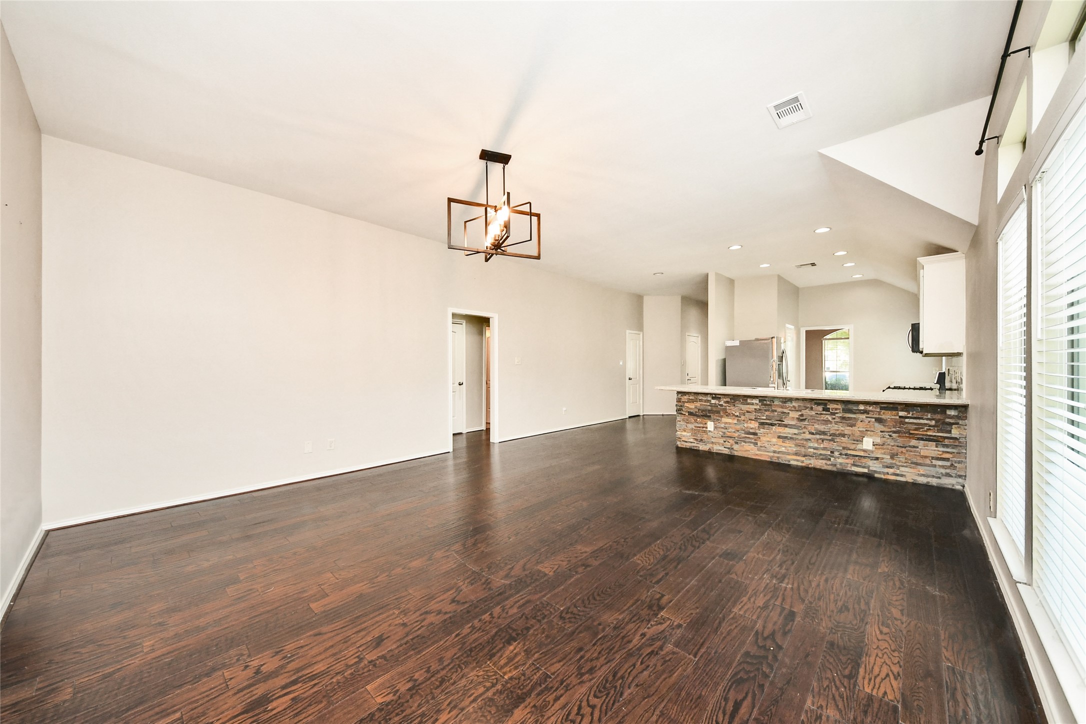 Spacious open-concept living area with elegant dark hardwood floors and a modern kitchen featuring a stylish stone-accented island, ideal for entertaining.