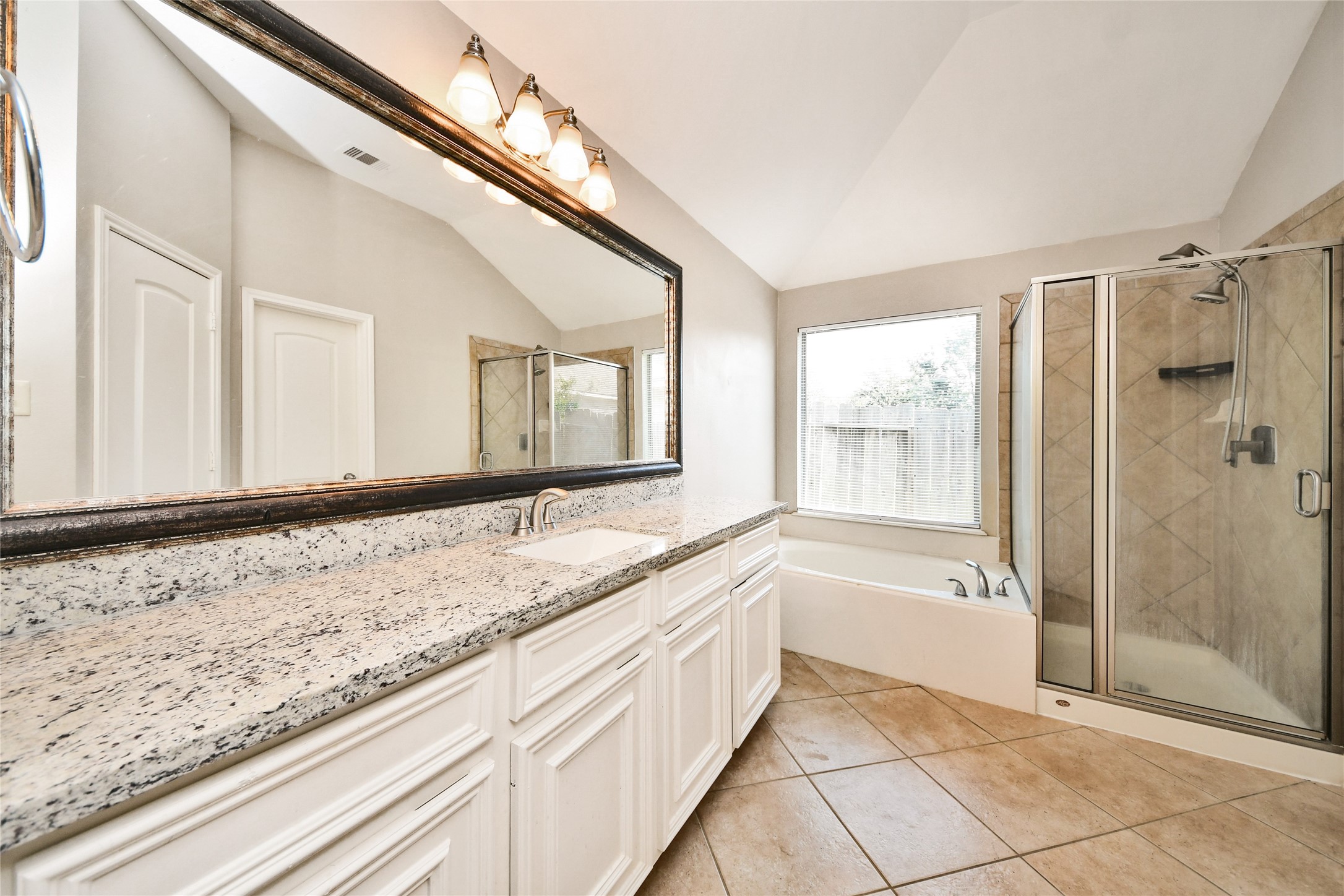 Elegant bathroom featuring a spacious granite countertop with dual sinks, a large framed mirror, and a luxurious glass-enclosed shower alongside a relaxing tub.