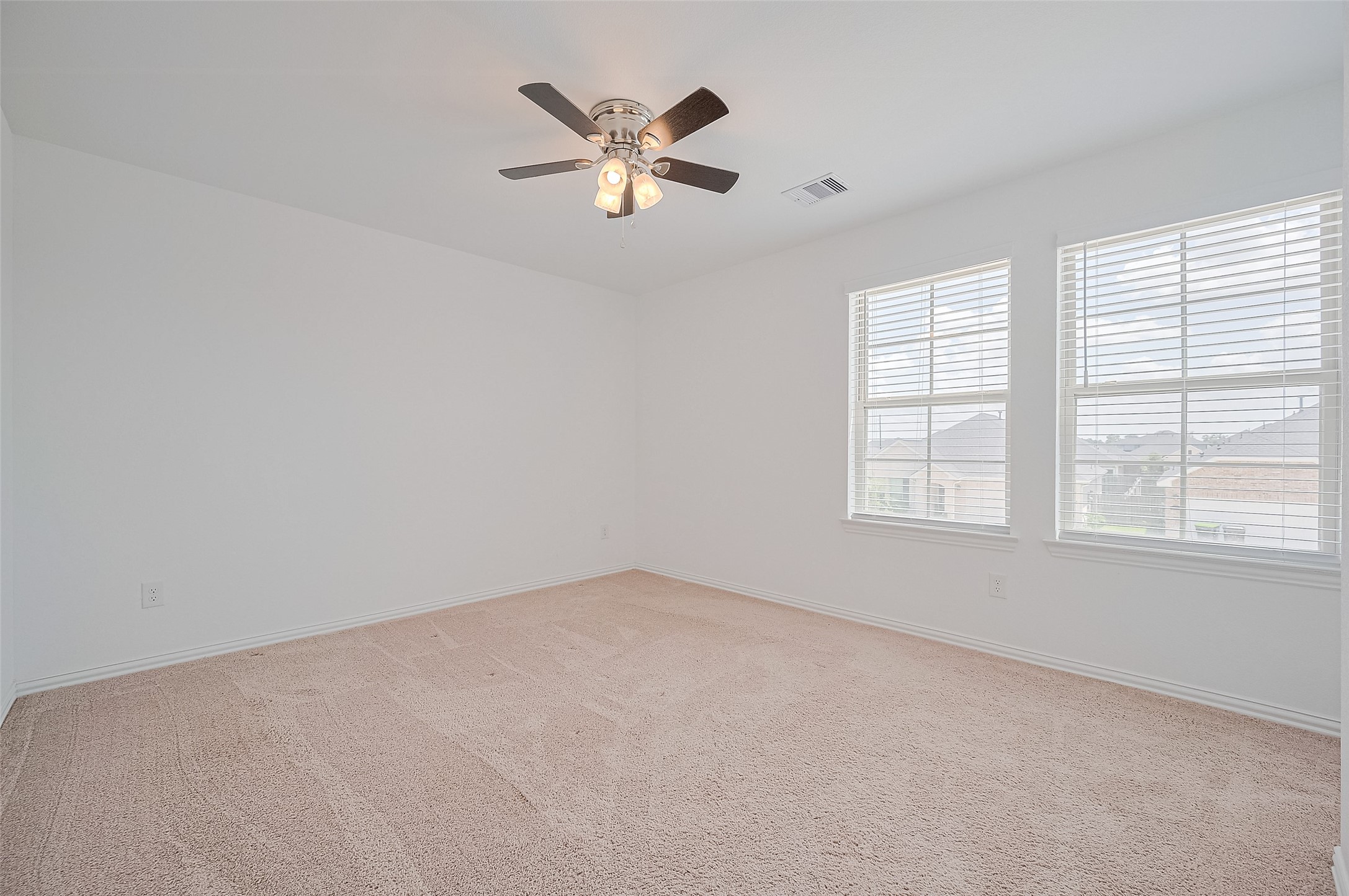 Bright, spacious room with neutral carpeting and a ceiling fan.