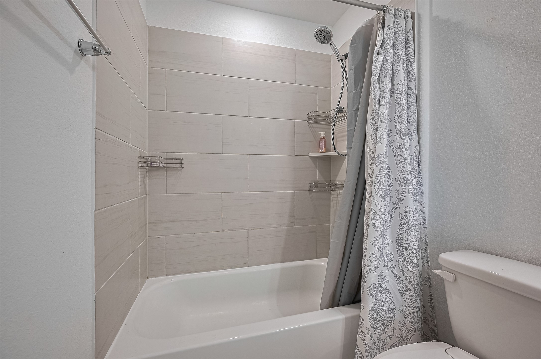 A tiled shower and bathtub, featuring a patterned curtain and built-in shelves.