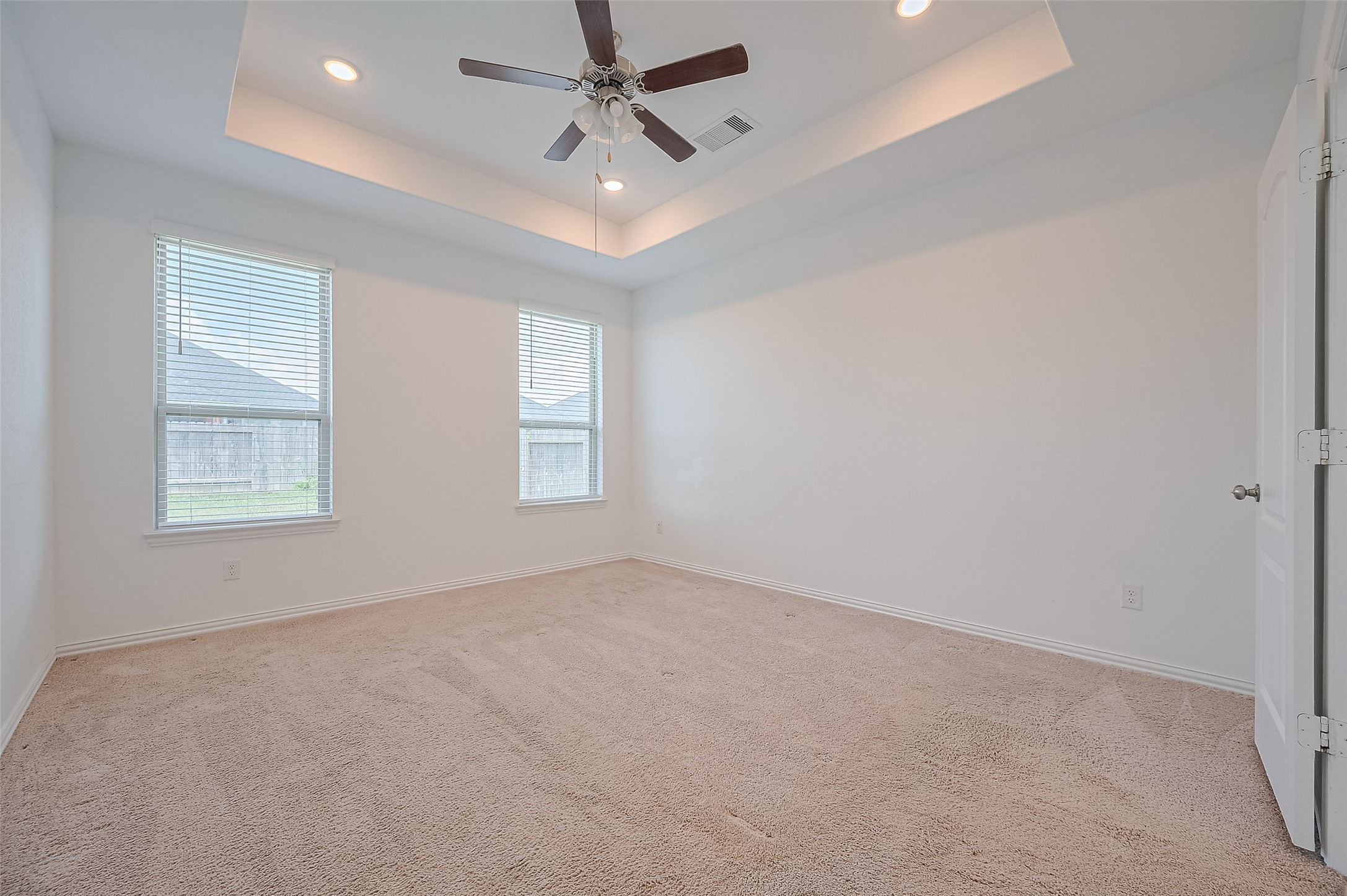 Primary bedroom features plush carpeting and a tray ceiling with recessed lighting.