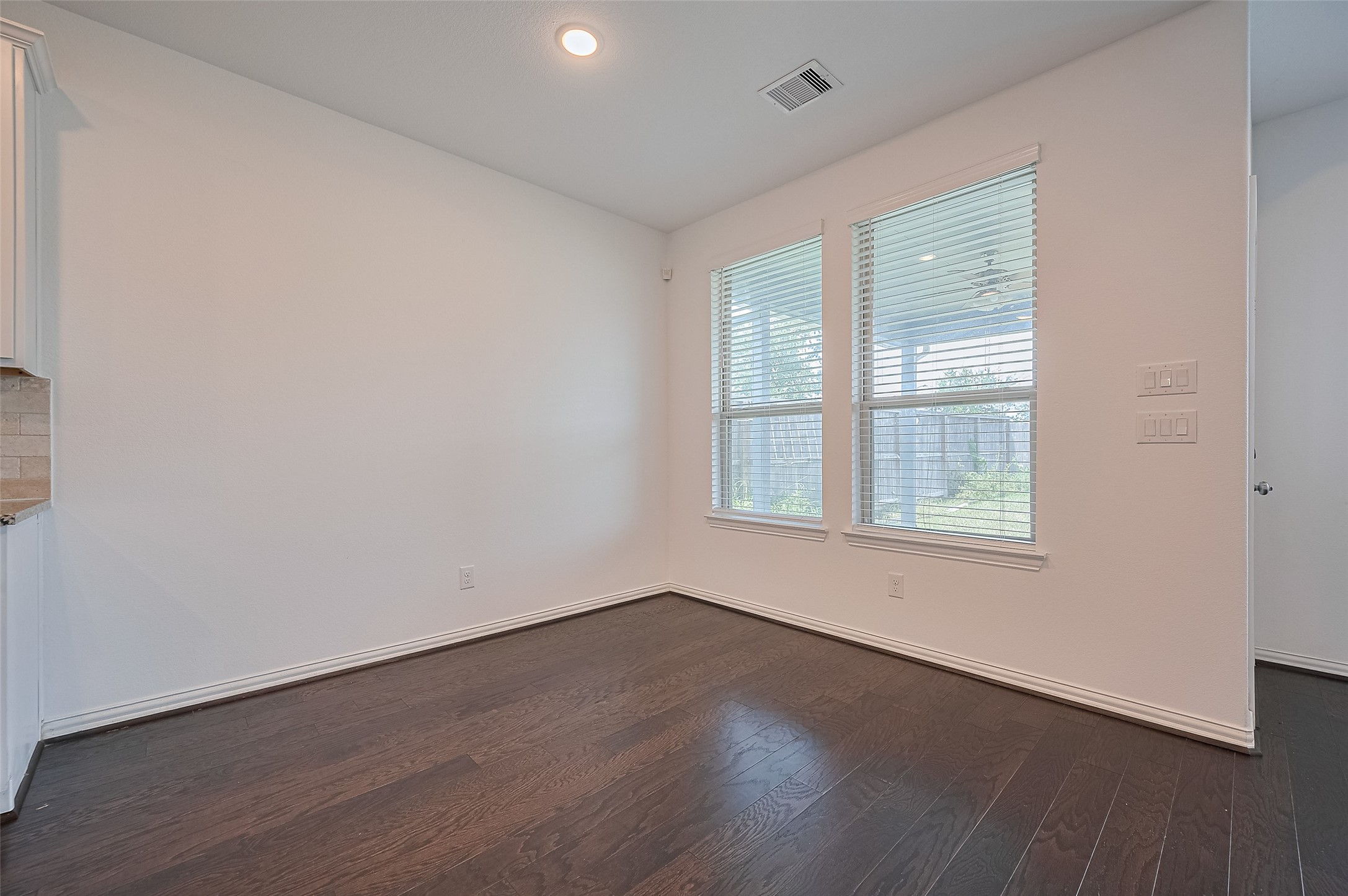 Bright and spacious dining area featuring two windows and wooden floor.